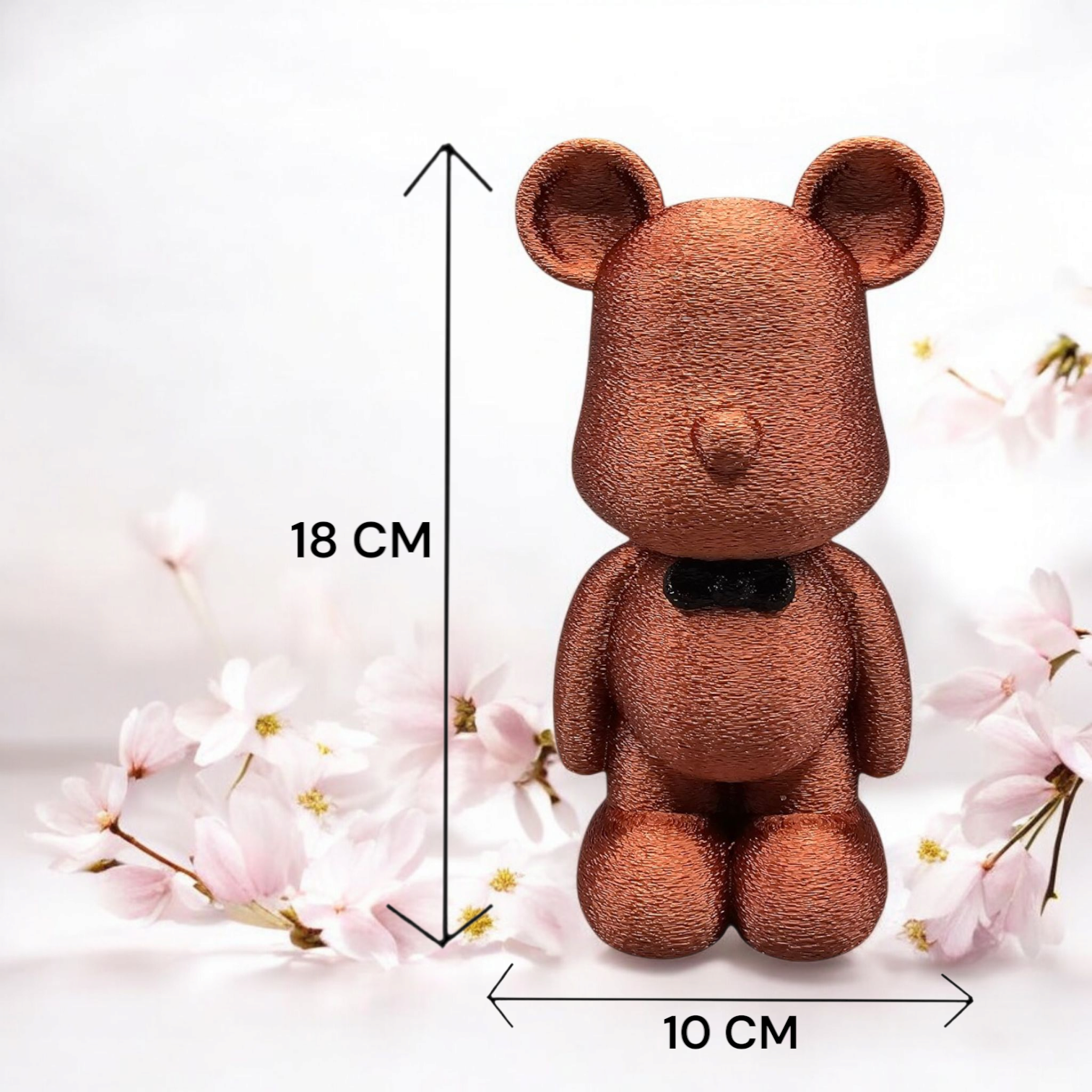 Bronzen teddybeerfiguurtje met een vlinderdasje, 18 cm hoog en 10 cm breed, met een bloemenachtergrond.