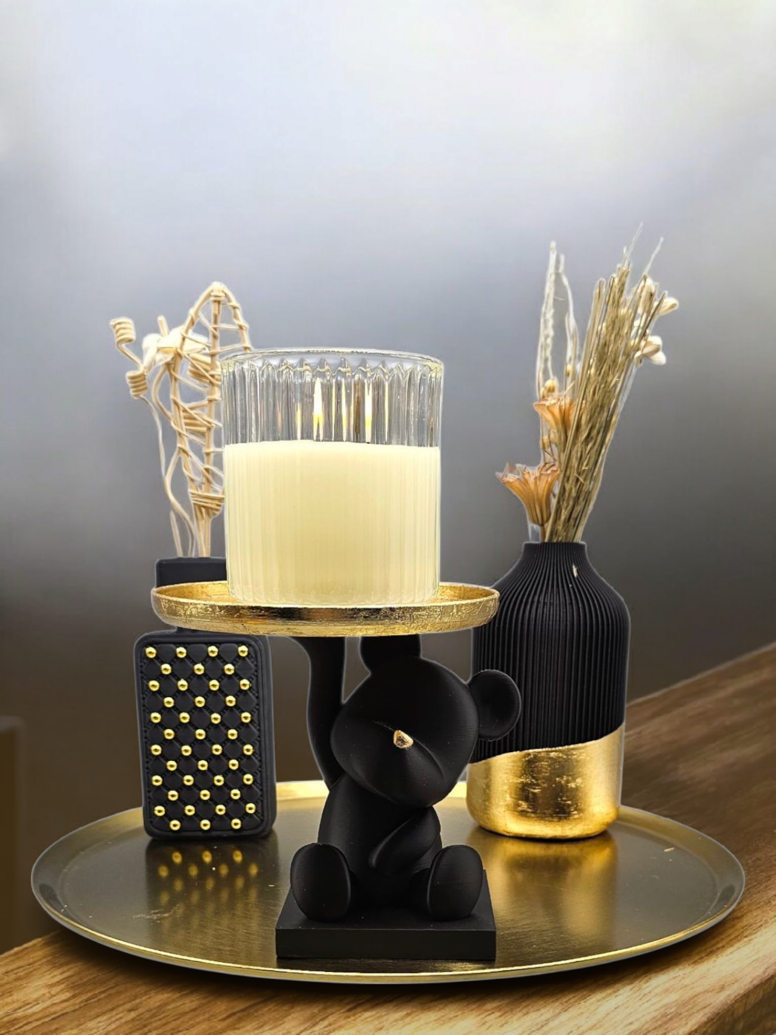 Een beeldje van een zwarte beer die een gouden dienblad met een kaars vasthoudt, plus vazen ​​en versieringen op een gouden dienblad.