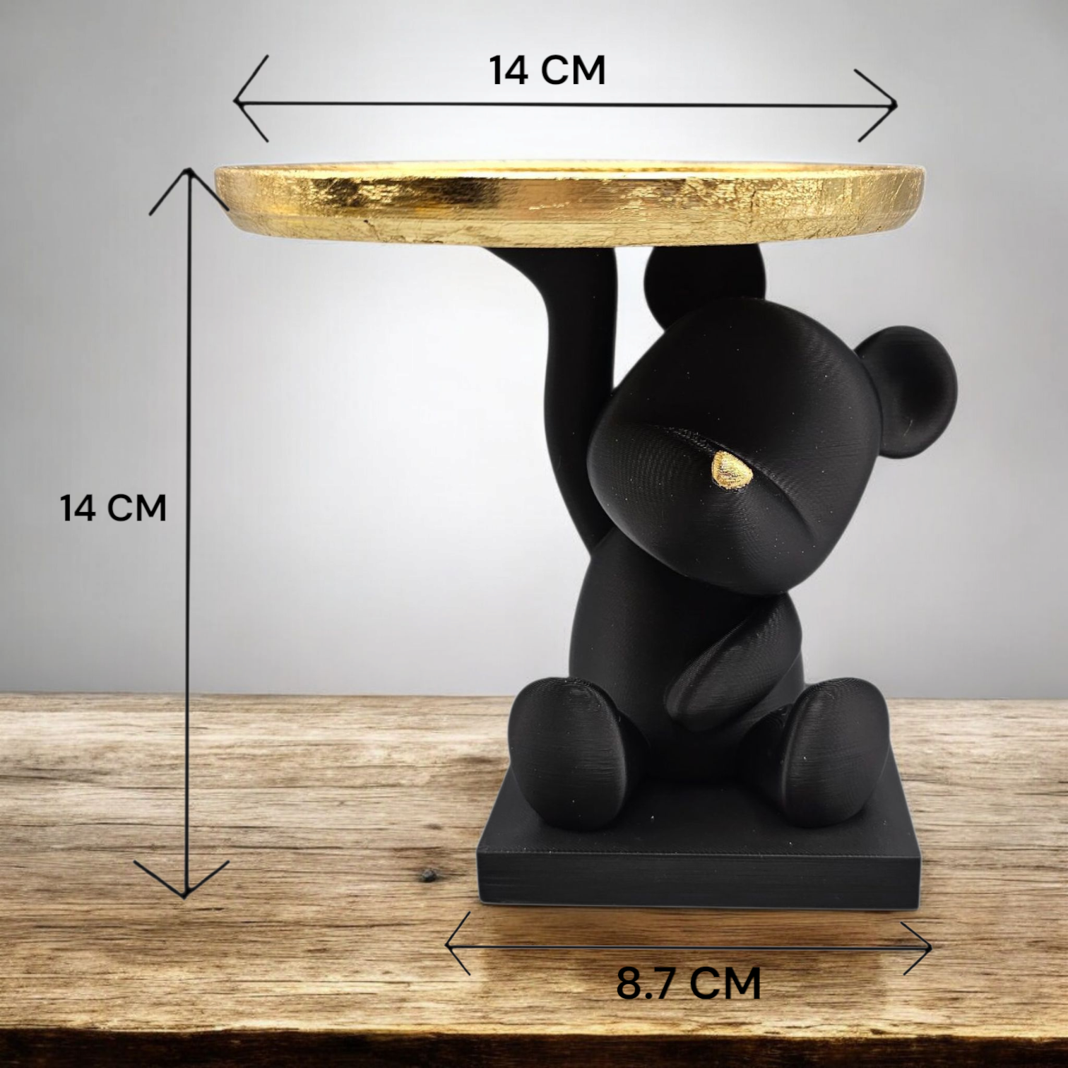 Een beeldje van een zwarte beer die een gouden dienblad met een kaars vasthoudt, plus vazen ​​en versieringen op een gouden dienblad.