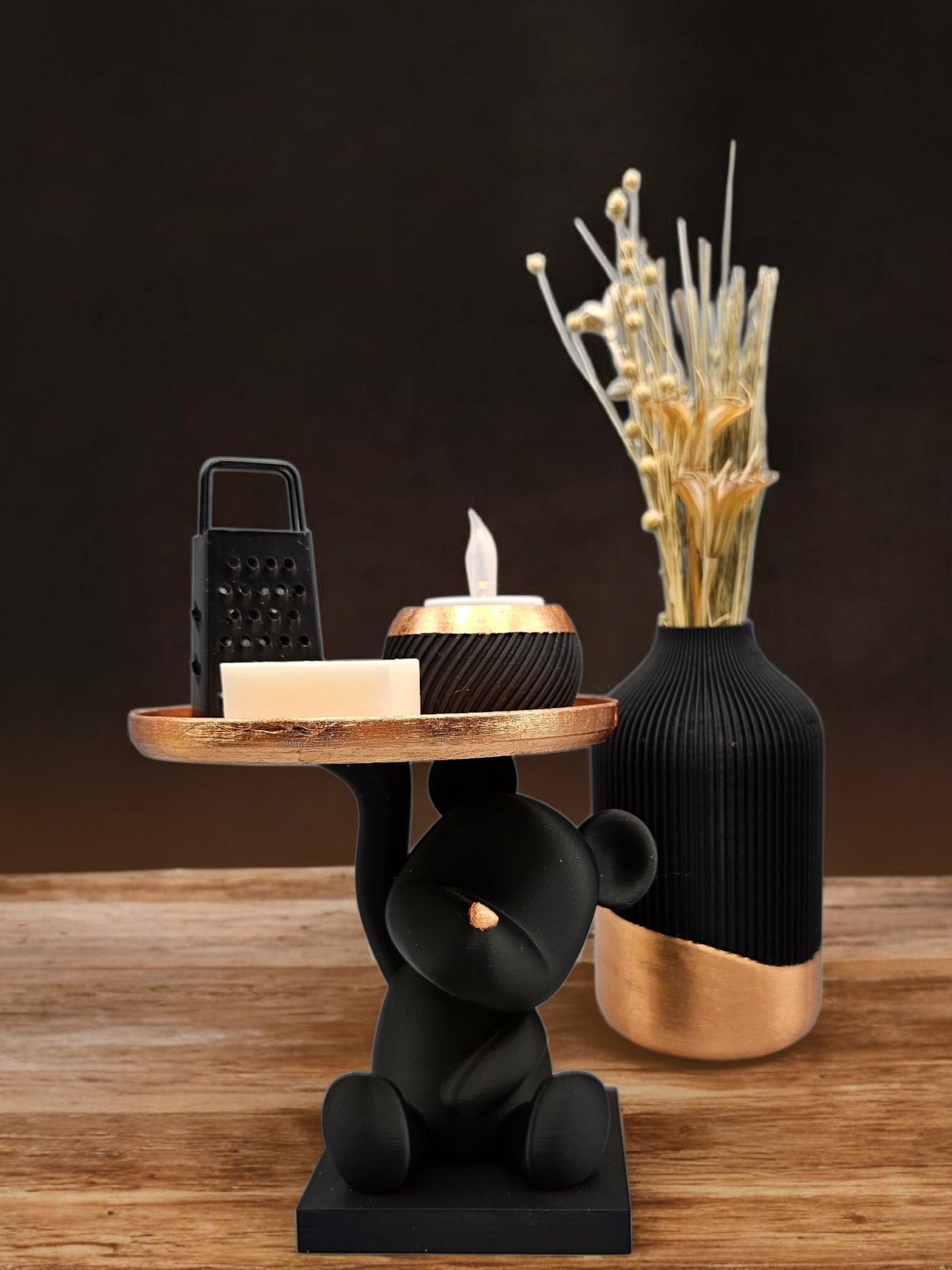 Een tafel in de vorm van een zwarte beer met een dienblad waarop een kaars, een rasp en zeep staan; daarnaast een vaas met bloemen.