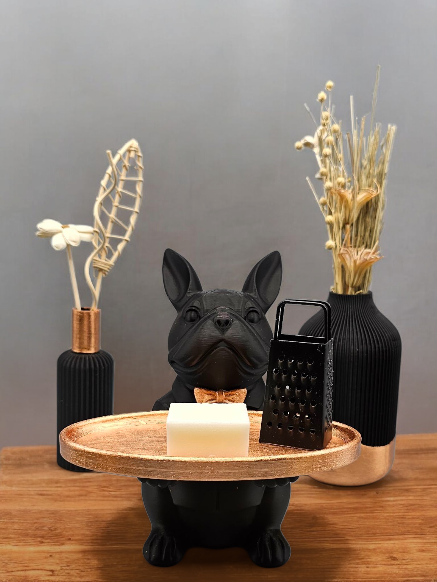 Een beeld van een zwarte bulldog die een gouden dienblad met zeep en een rasp vasthoudt; decoratieve vazen ​​op de achtergrond.