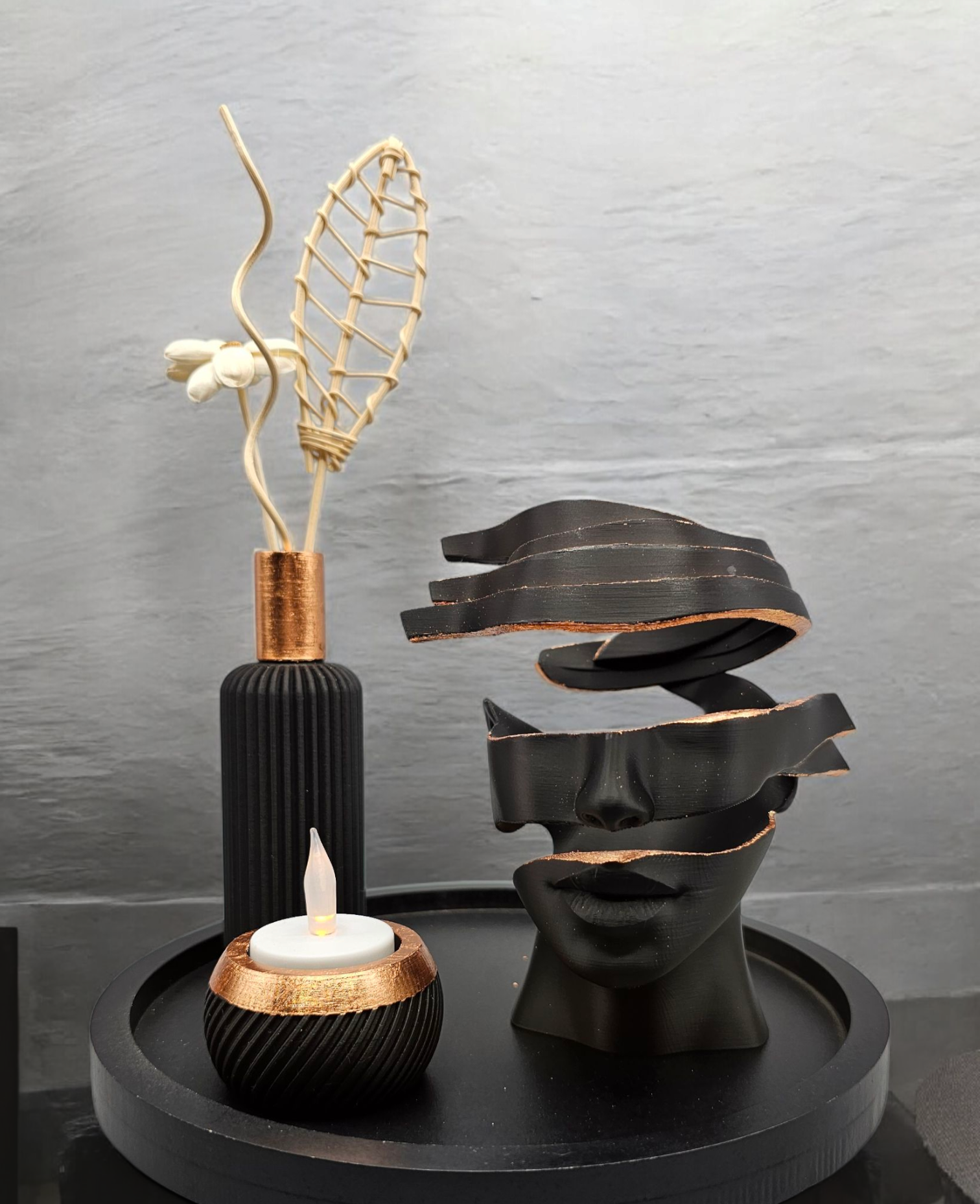 Decoratie in zwart en goud: sculptuur van een doorgesneden gezicht, kaars, vaas met een arrangement van gedroogde bloemen op een dienblad.