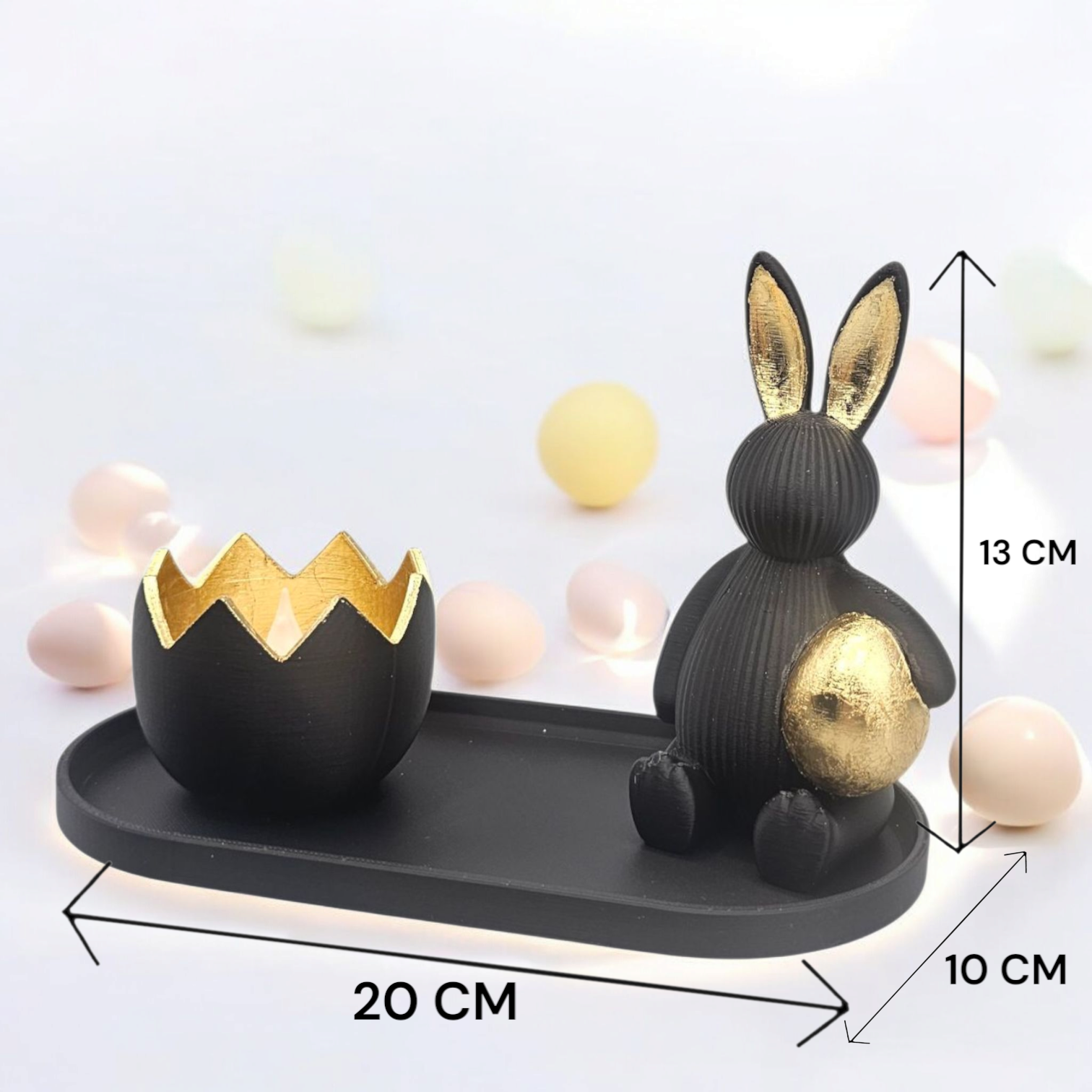 Een zwart konijn met een gouden ei in zijn handen, naast een eivormige kom met een gouden binnenkant, op een dienblad met paaseieren en bloemen.