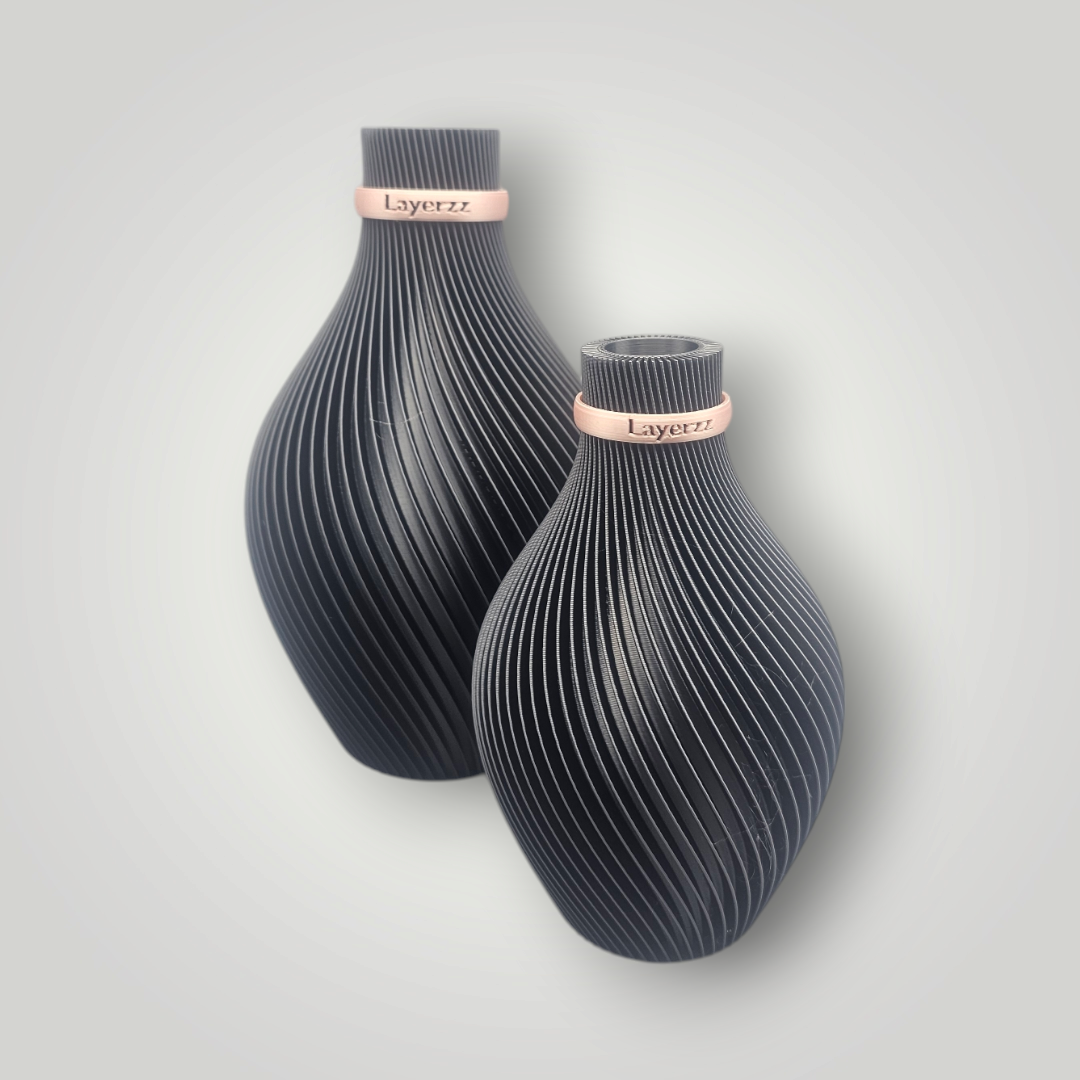 Twee zwarte, gestructureerde vazen ​​met roségouden banden rond de hals, tegen een lichtgrijze achtergrond.