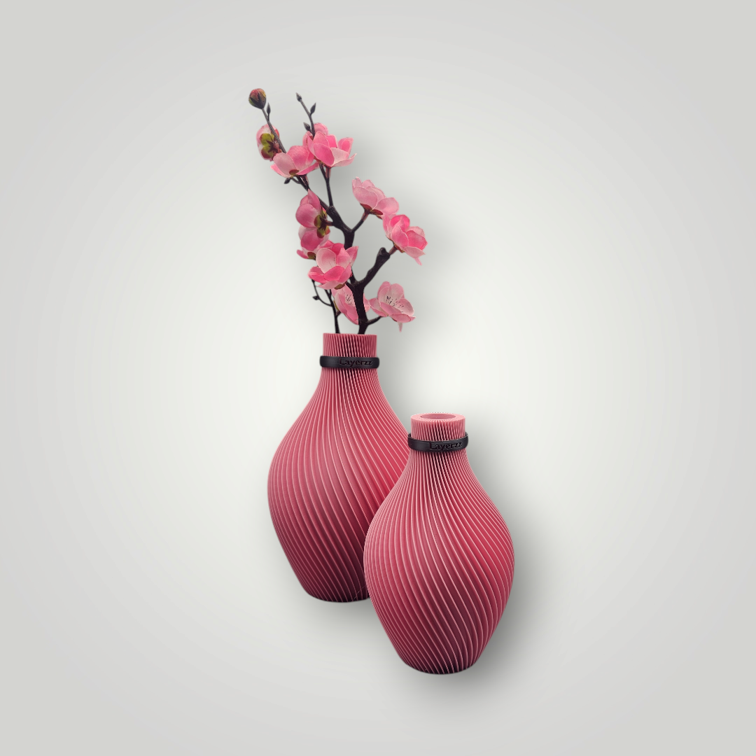 Twee roze vazen ​​met een patroon, gevuld met roze bloemen, tegen een witte muur.