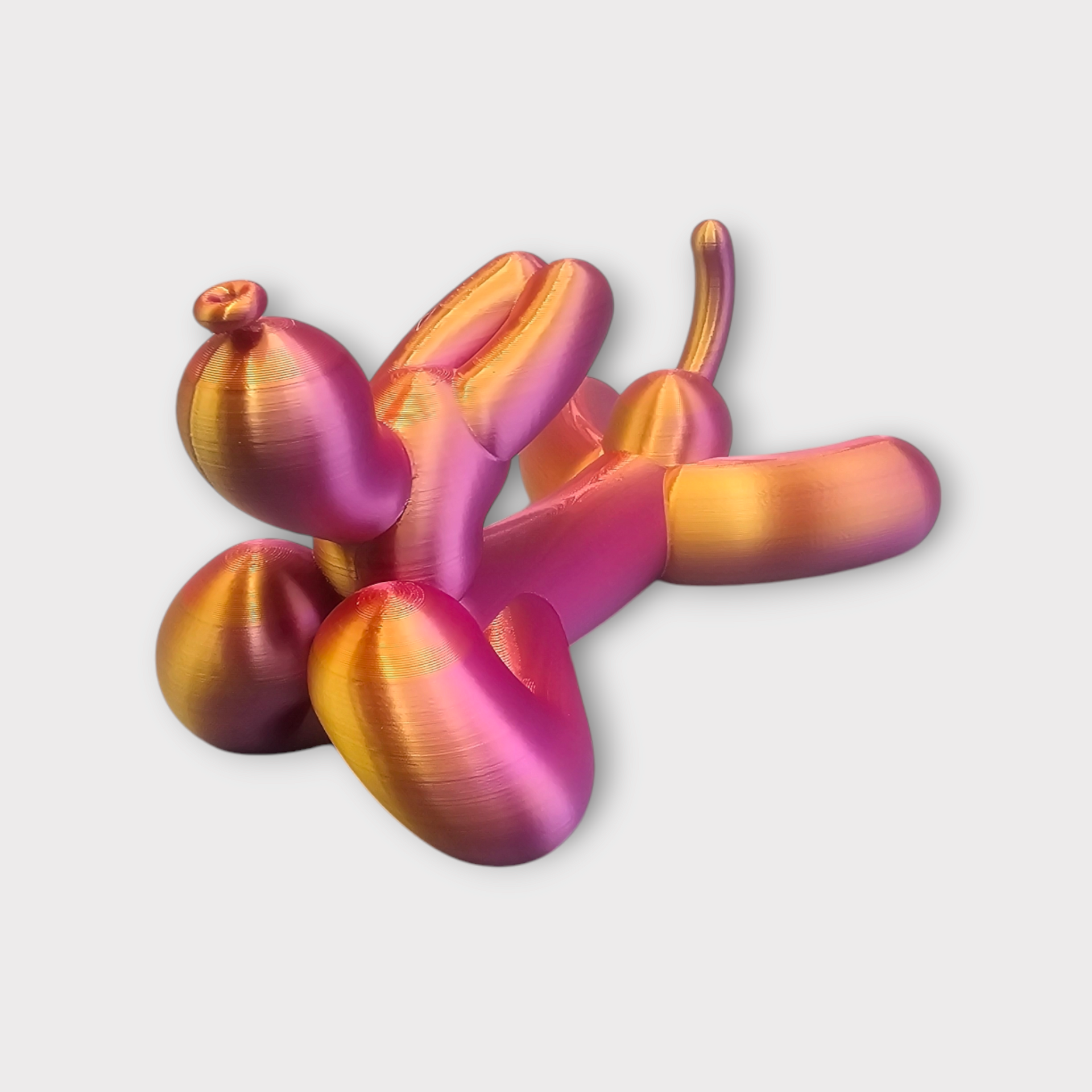 3D-geprint ballonfiguur in iriserend roze en goud, liggend op een witte achtergrond.