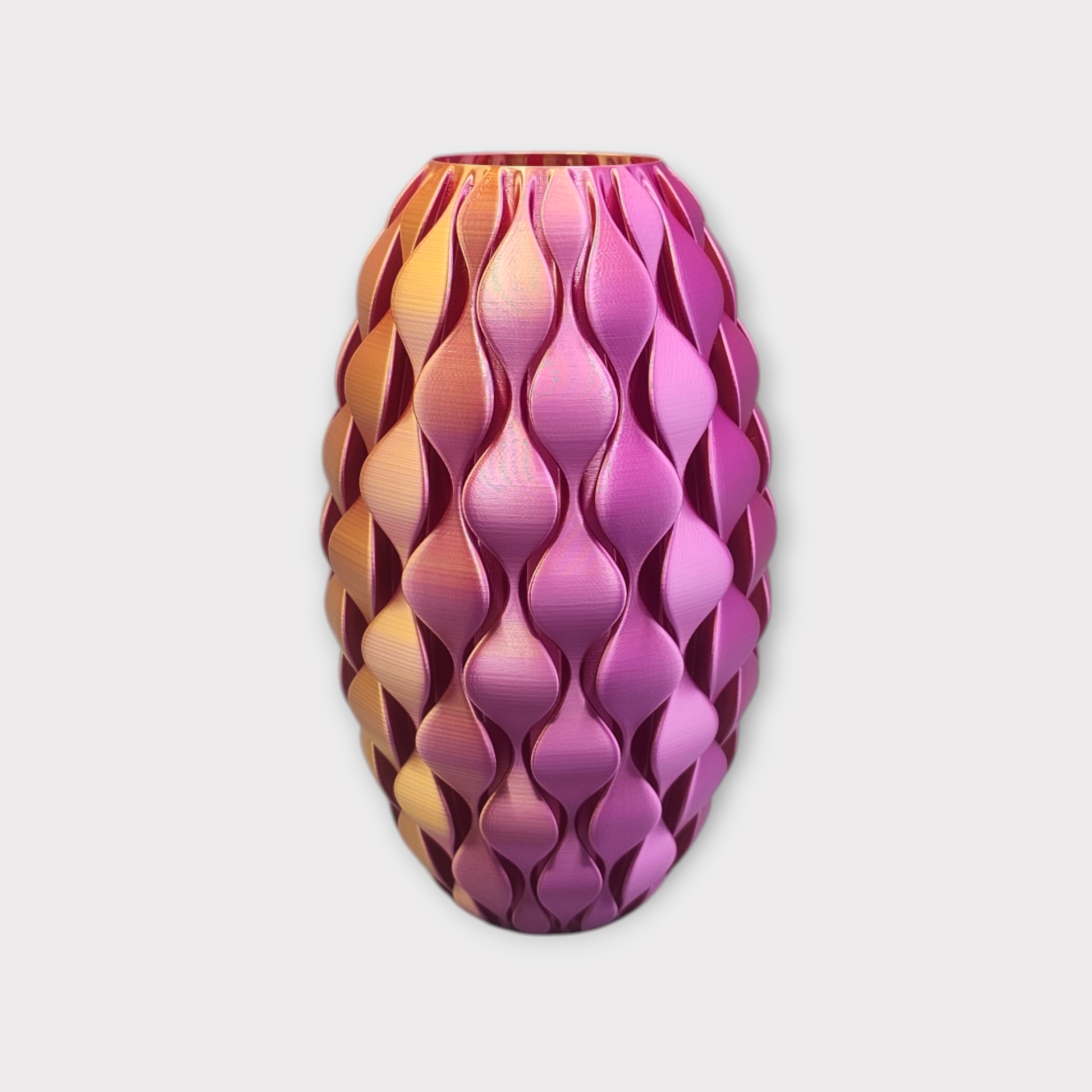 Een 3D-geprinte vaas met een ombré-effect en een herhalend druppelvormig patroon in goud-, roze- en paarse tinten.