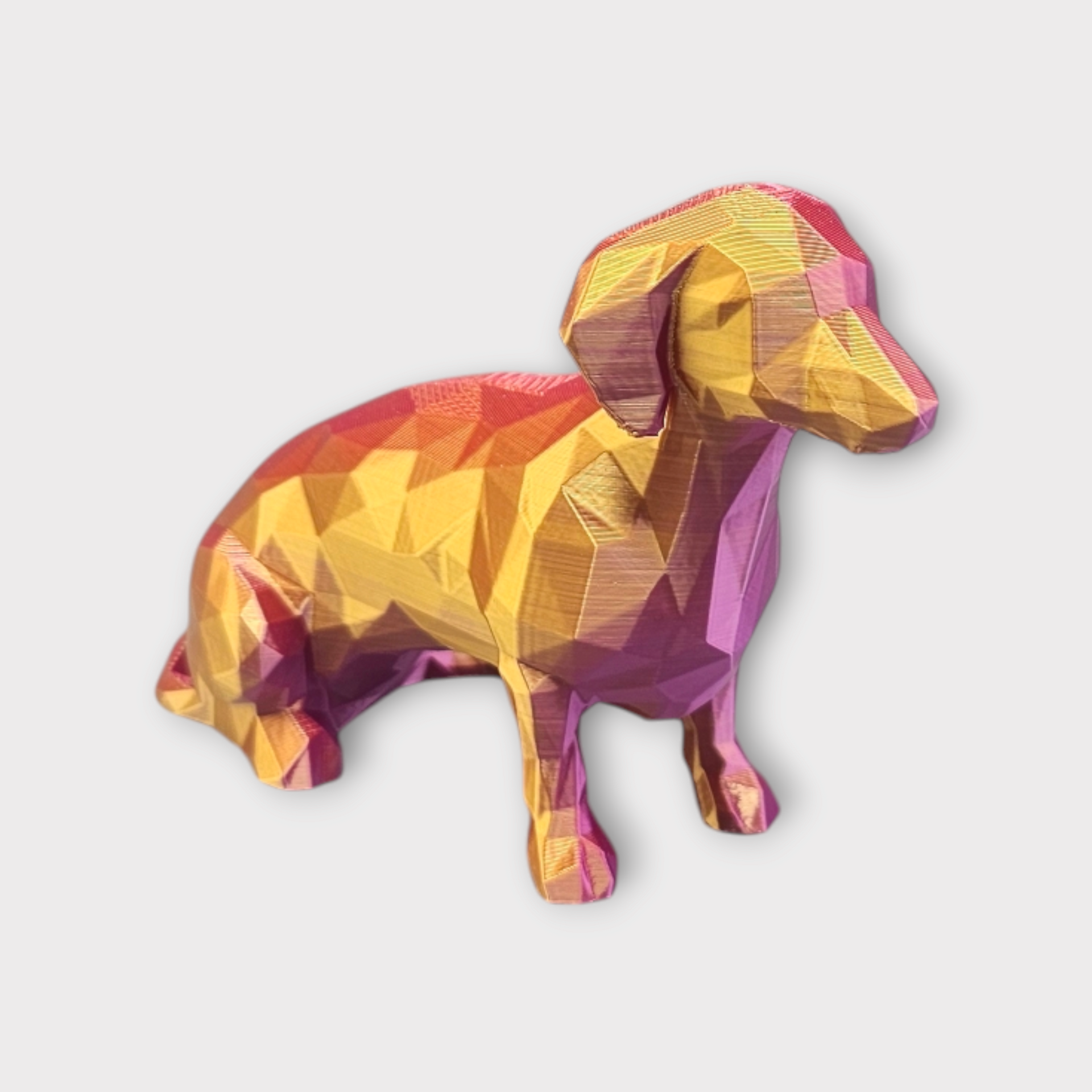 Veelhoekige teckelsculptuur met een kleurverloop van goud en roze.