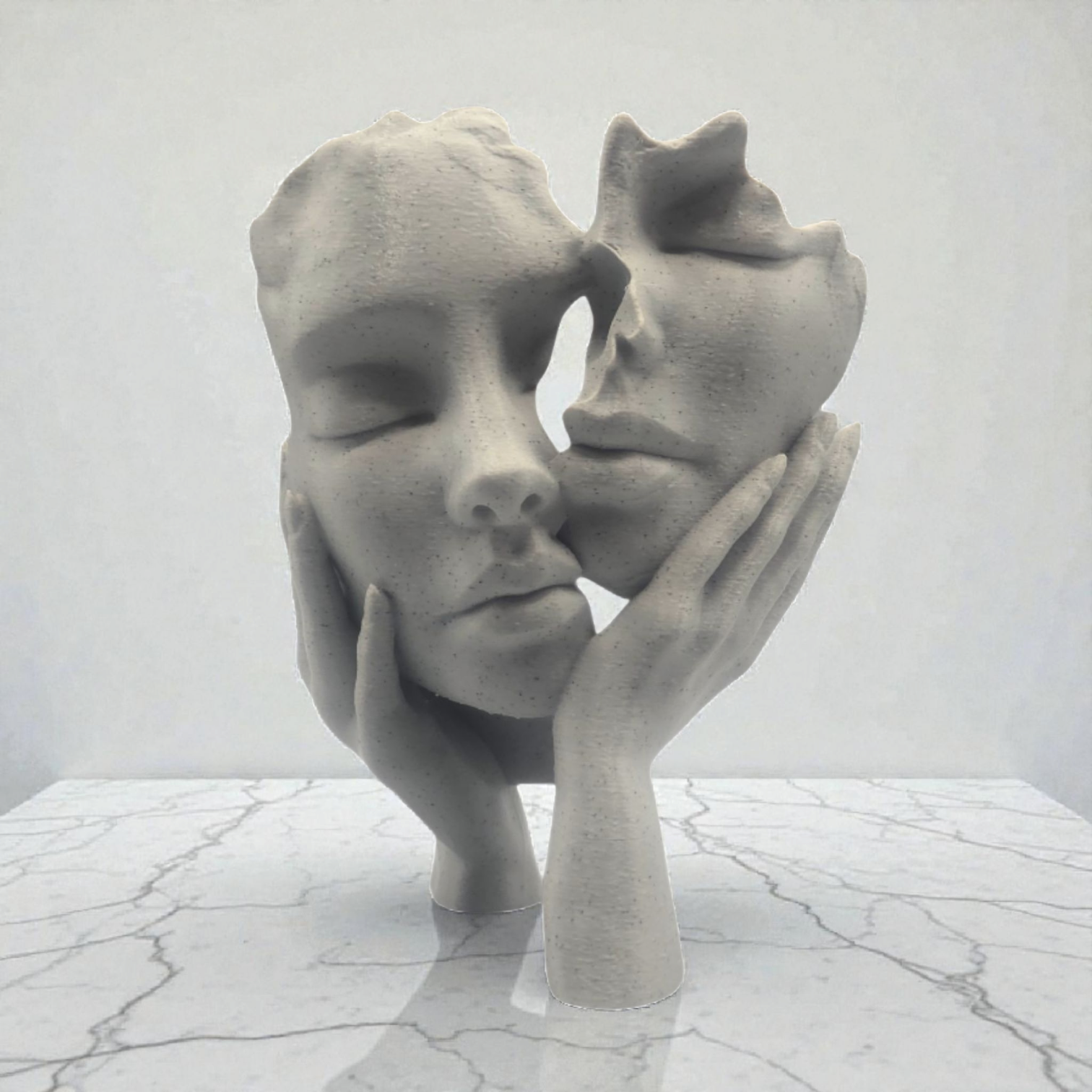 Een sculptuur van twee gezichten, waarvan er één de ander kust en die door handen worden vastgehouden, op een marmeren tafel.