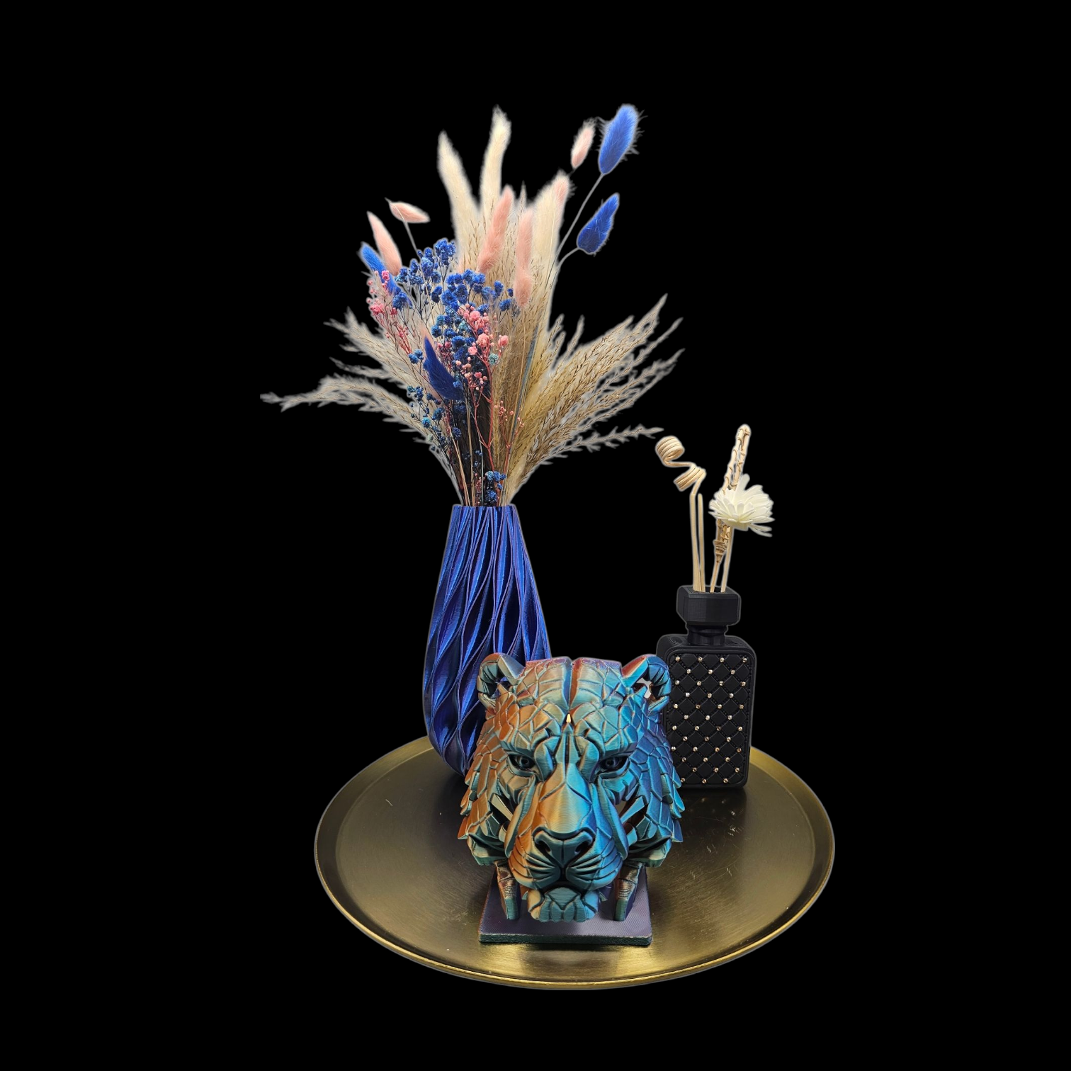 Een gouden dienblad met daarop een blauwe vaas met gedroogde bloemen, een beeldje van een tijgerkop en een zwarte vaas met stippen.