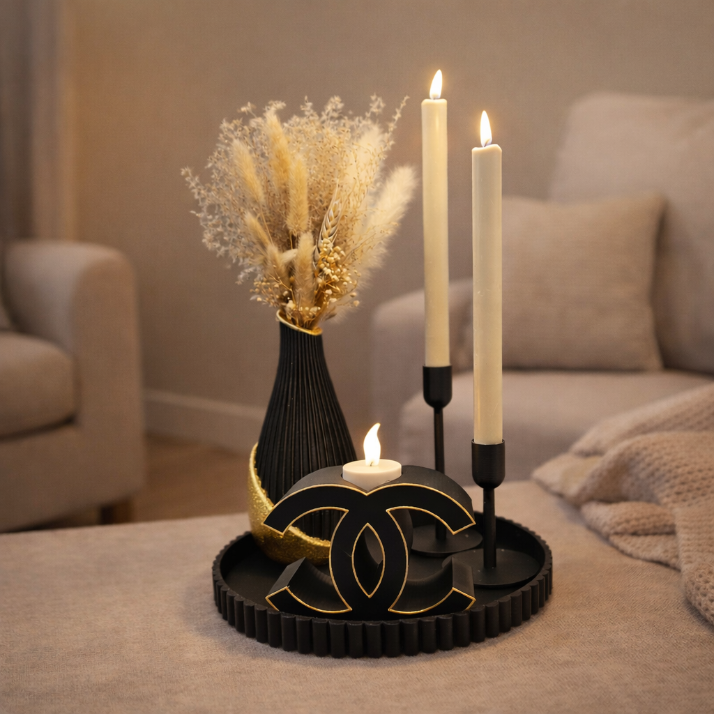 Een decoratief zwart dienblad met een vaas met gedroogde bloemen, twee hoge kaarsen en een kaarsenhouder met het Chanel-logo.