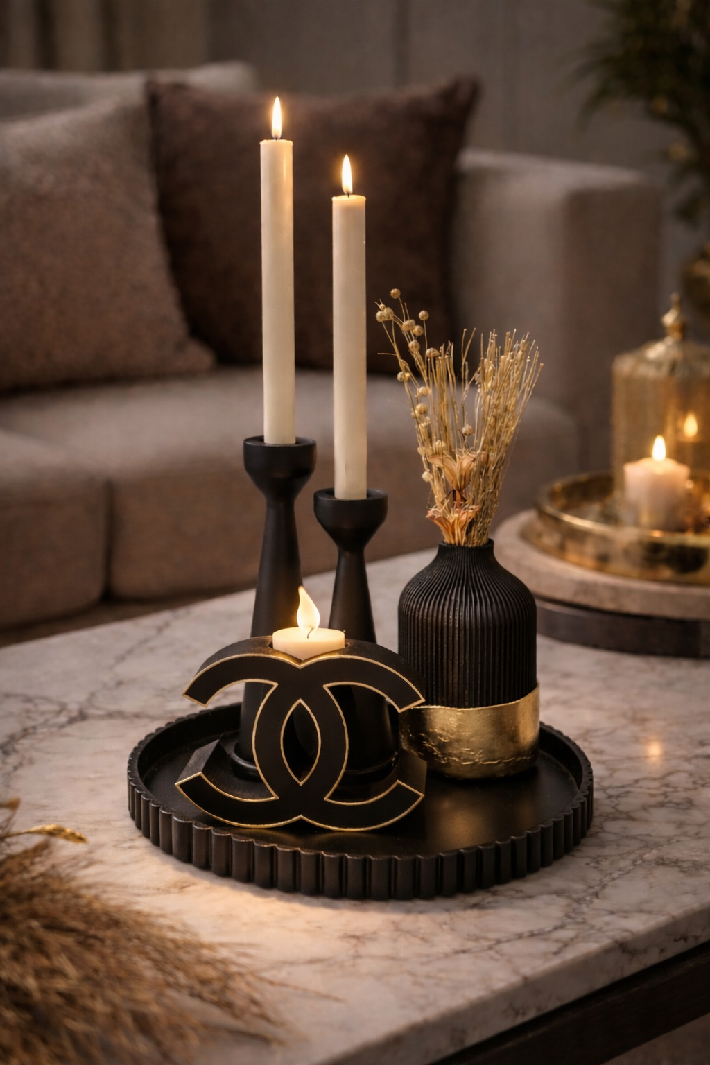 Salontafel met kaarsen, zwart dienblad, Chanel-logo en decoratieve vaas. Warme verlichting, neutrale tinten.