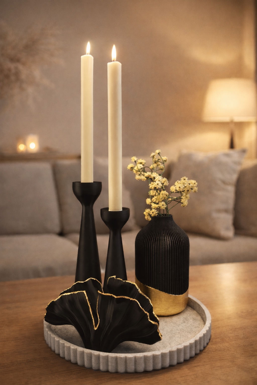 Een tafelstuk met twee zwarte kaarsen, een kleine zwart-gouden vaas met bloemen en een zwart decoratief item met ruches.