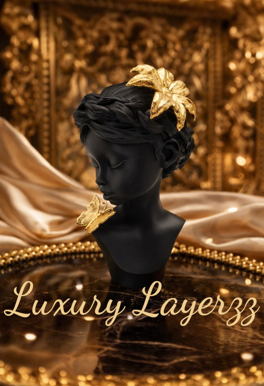 Een matzwarte buste, versierd met gouden haaraccessoires en een gouden halsketting, geplaatst tegen een achtergrond van gedrapeerd satijn en een dienblad met kralen.