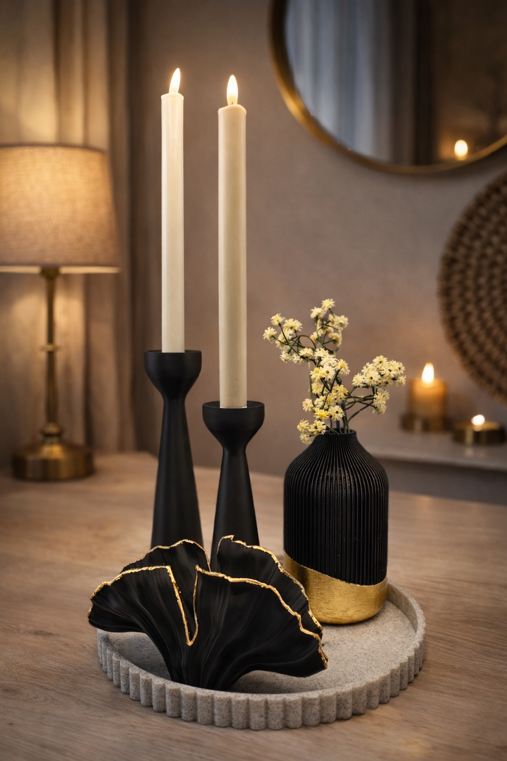 Een tafelstuk met twee zwarte kaarsen, een kleine zwart-gouden vaas met bloemen en een zwart decoratief item met ruches.