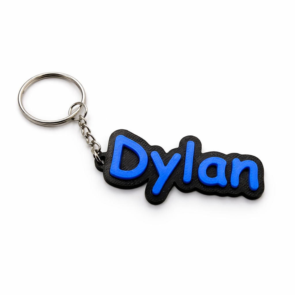 Een zwart-blauwe sleutelhanger met de tekst "Dylan" in een gestileerd 3D-lettertype, bevestigd aan een metalen ring.