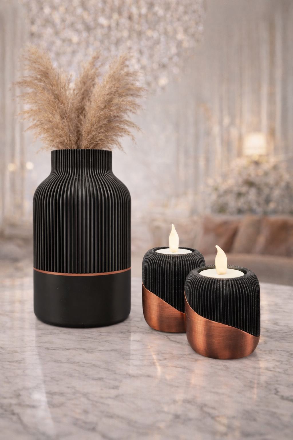 Zwarte en koperkleurige decoratieve objecten op een marmeren tafel: een vaas met pampasgras en twee kandelaars met nepkaarsen.