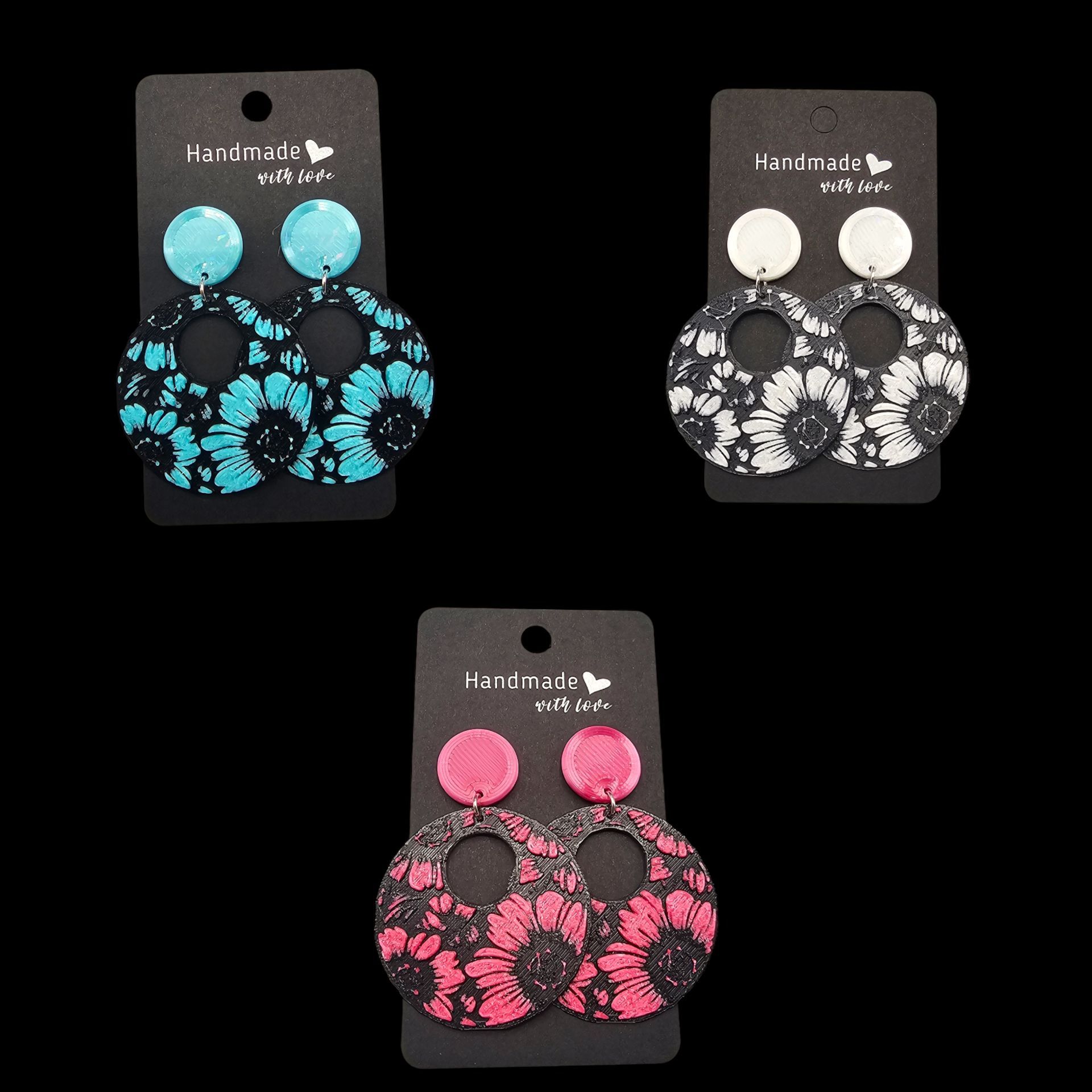 Drie paar hangende oorbellen, elk met een bloemmotief en verschillende gekleurde bovenkanten: turquoise, wit en roze.