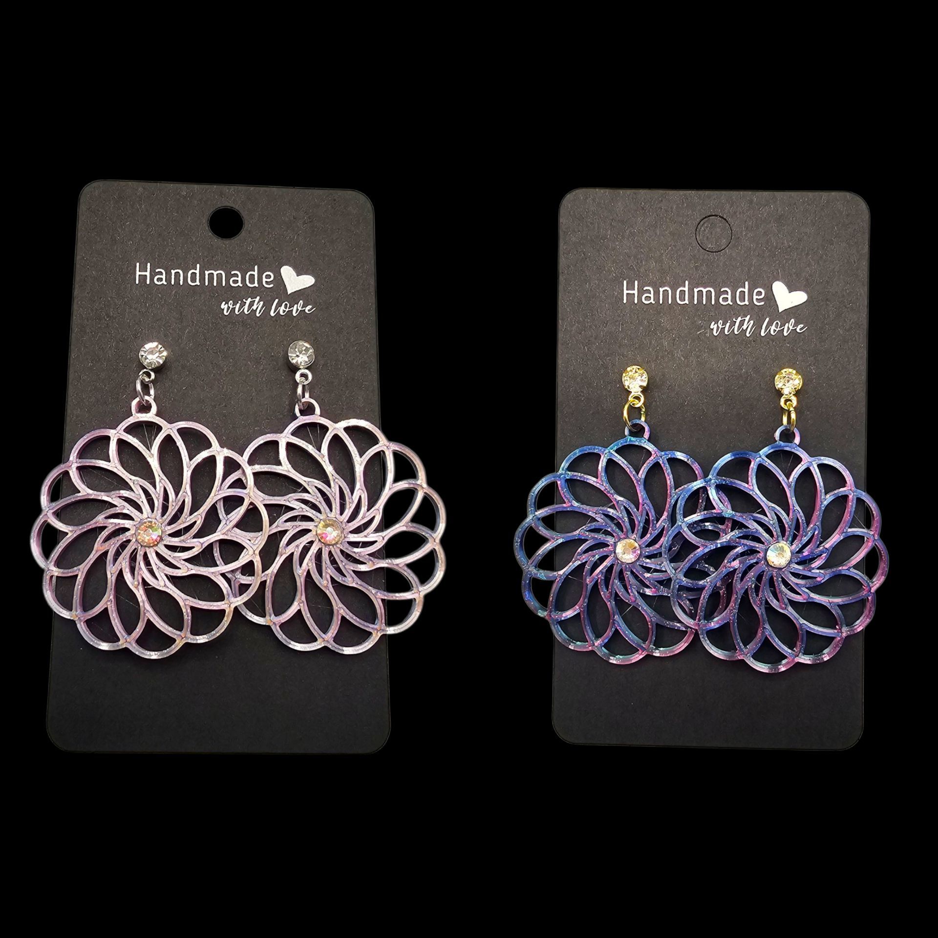 Twee paar glinsterende, bloemvormige oorbellen, een roze en een blauwe, gepresenteerd op zwarte oorbelkaartjes.