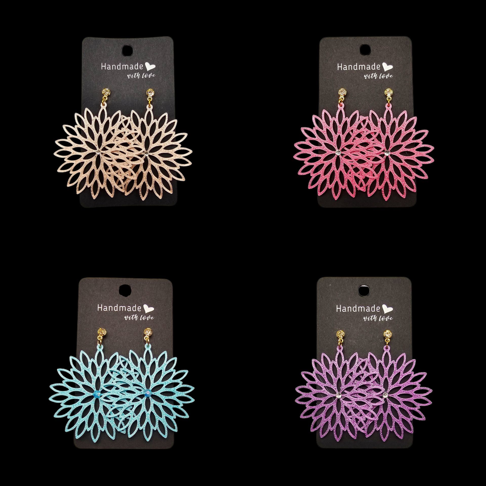 Vier paar bloemvormige oorbellen in lichtbruin, roze, turquoise en paars, op zwarte kaartjes met gouden haakjes.