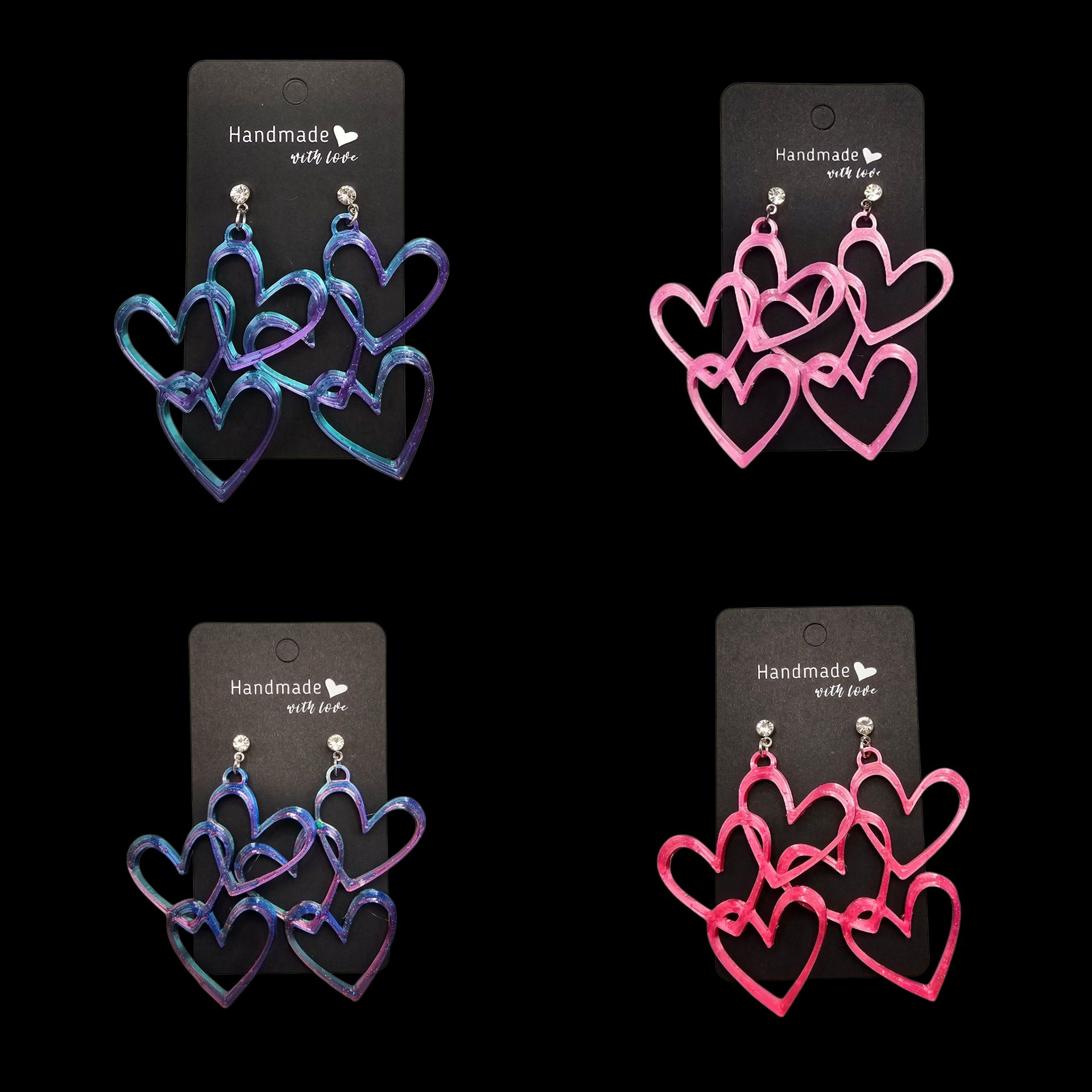 Vier paar glinsterende hartvormige oorbellen in blauw, roze en paars op zwarte kaartjes.