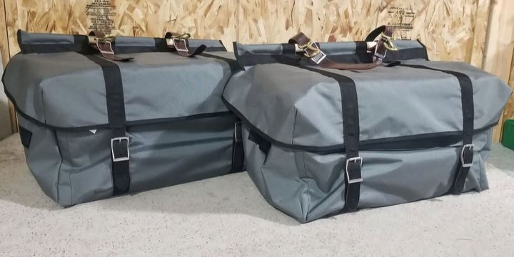Two grey, rectangular, weather-resistant storage bags with black buckle straps sitting on a light-colored surface.