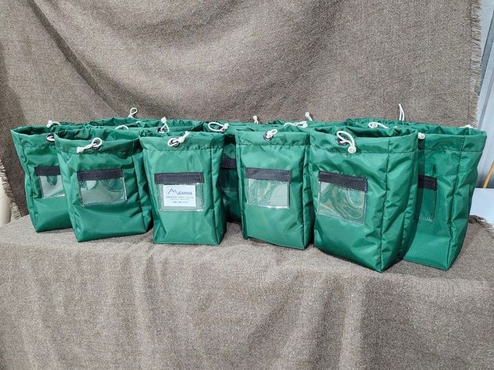 A row of green, drawstring storage bags with clear pockets, arranged on a tan, textured cloth surface.