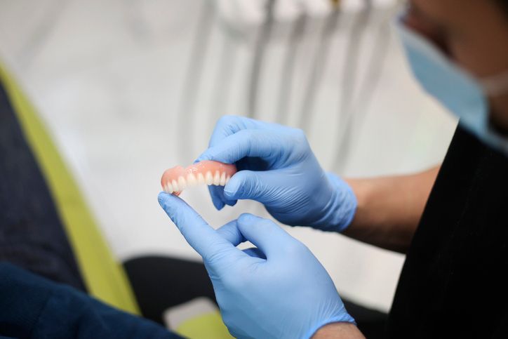 Dentist wearing gloves examines a set of upper dentures in a dental office.