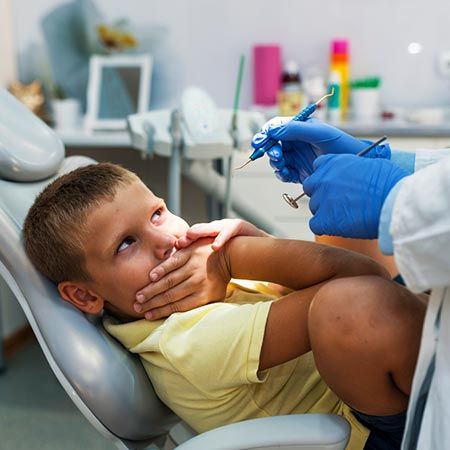 Young Child covering teeth while dentist administers Exam