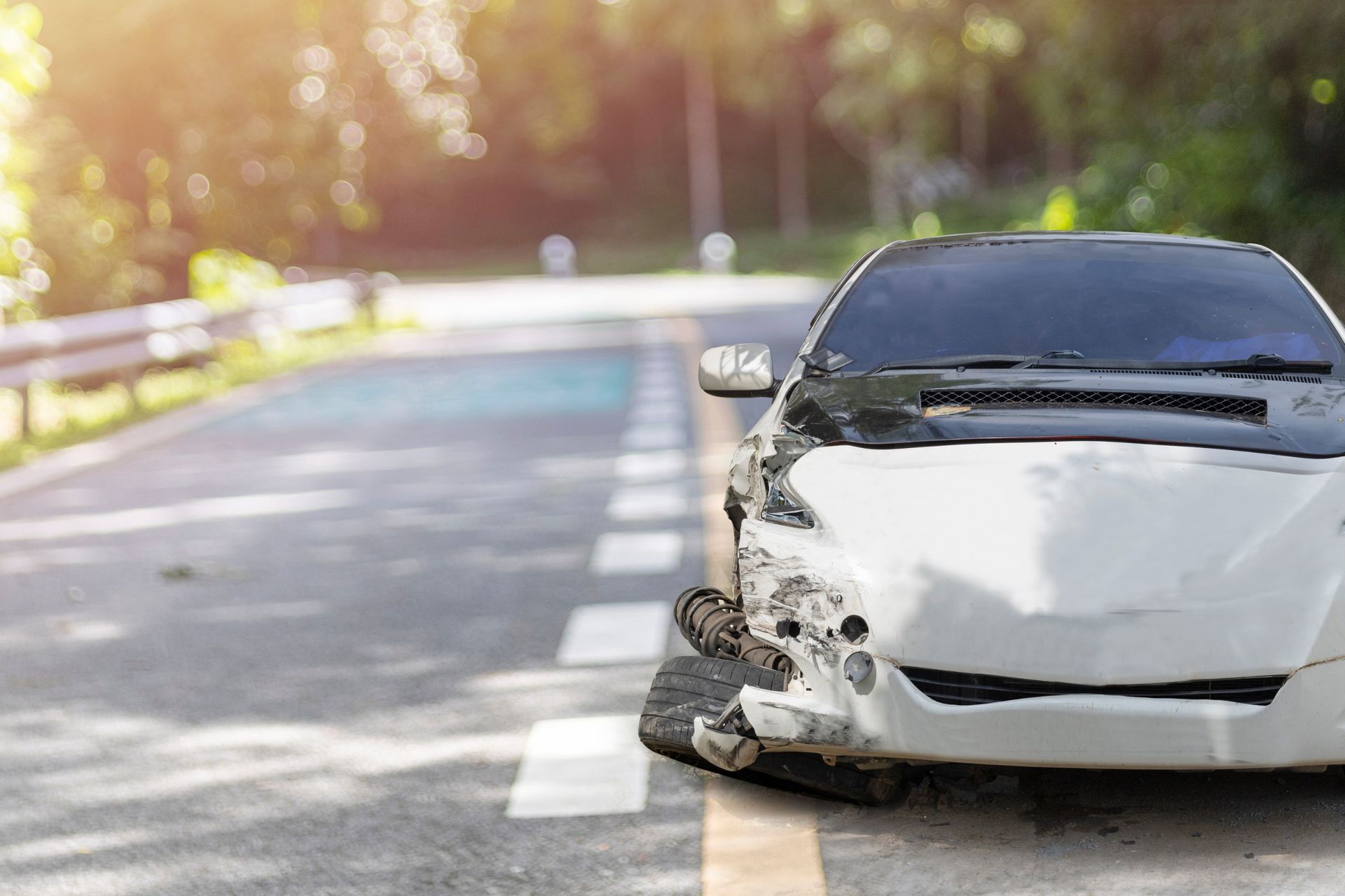 A white car with a damaged bumper is parked on the side of the road.