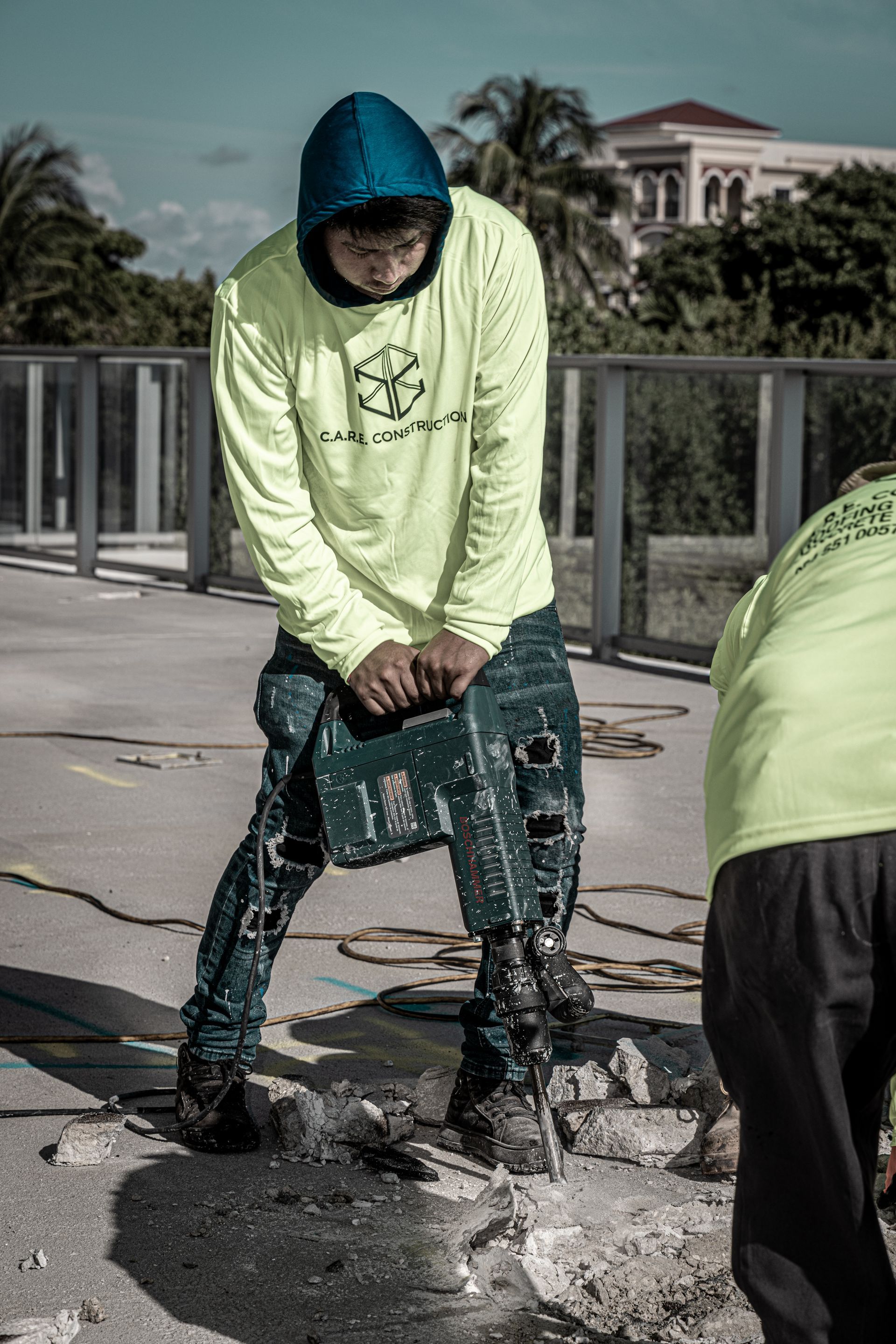 A man in a neon yellow shirt is using a hammer to break concrete.