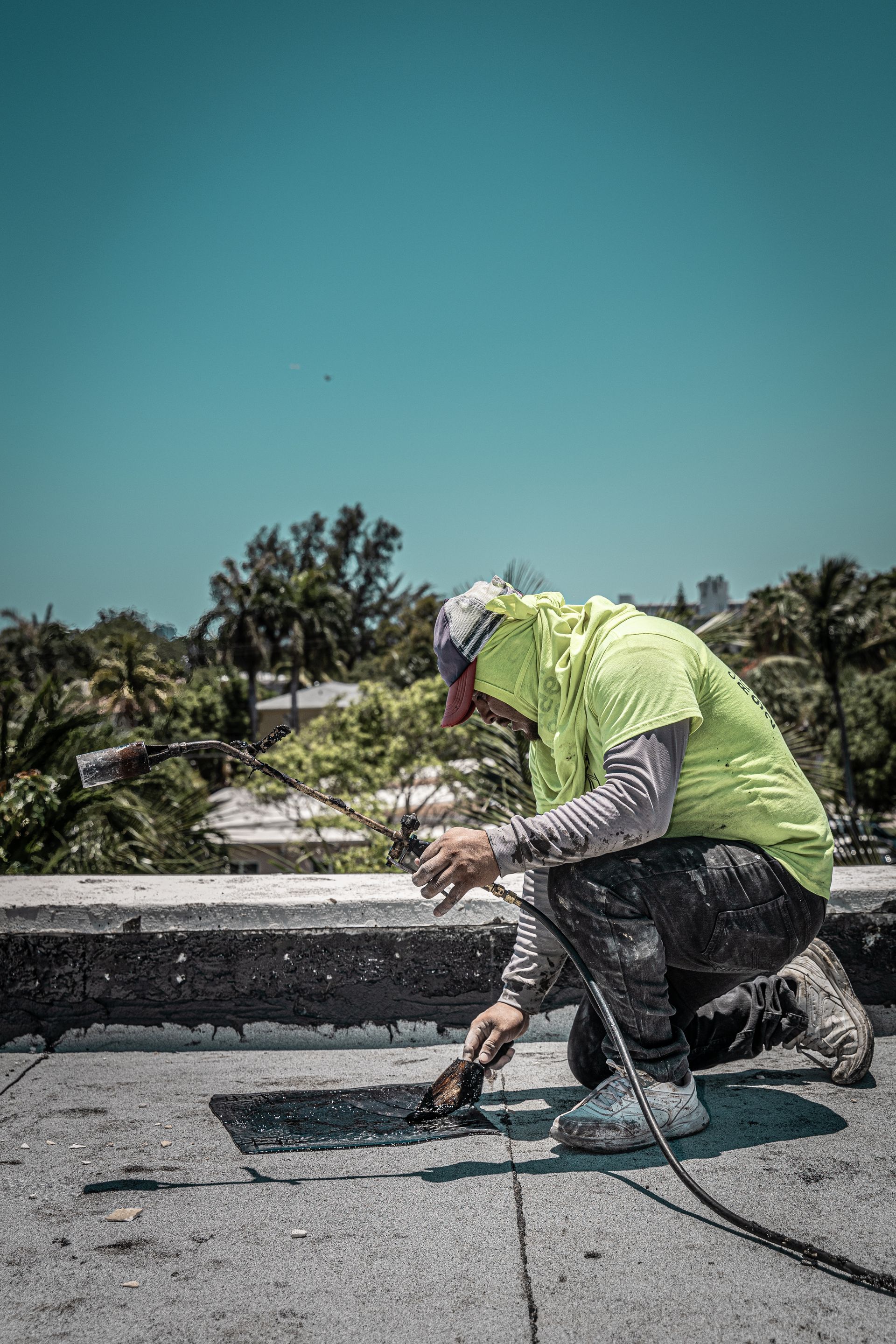 A man is kneeling down on a roof using a tool.