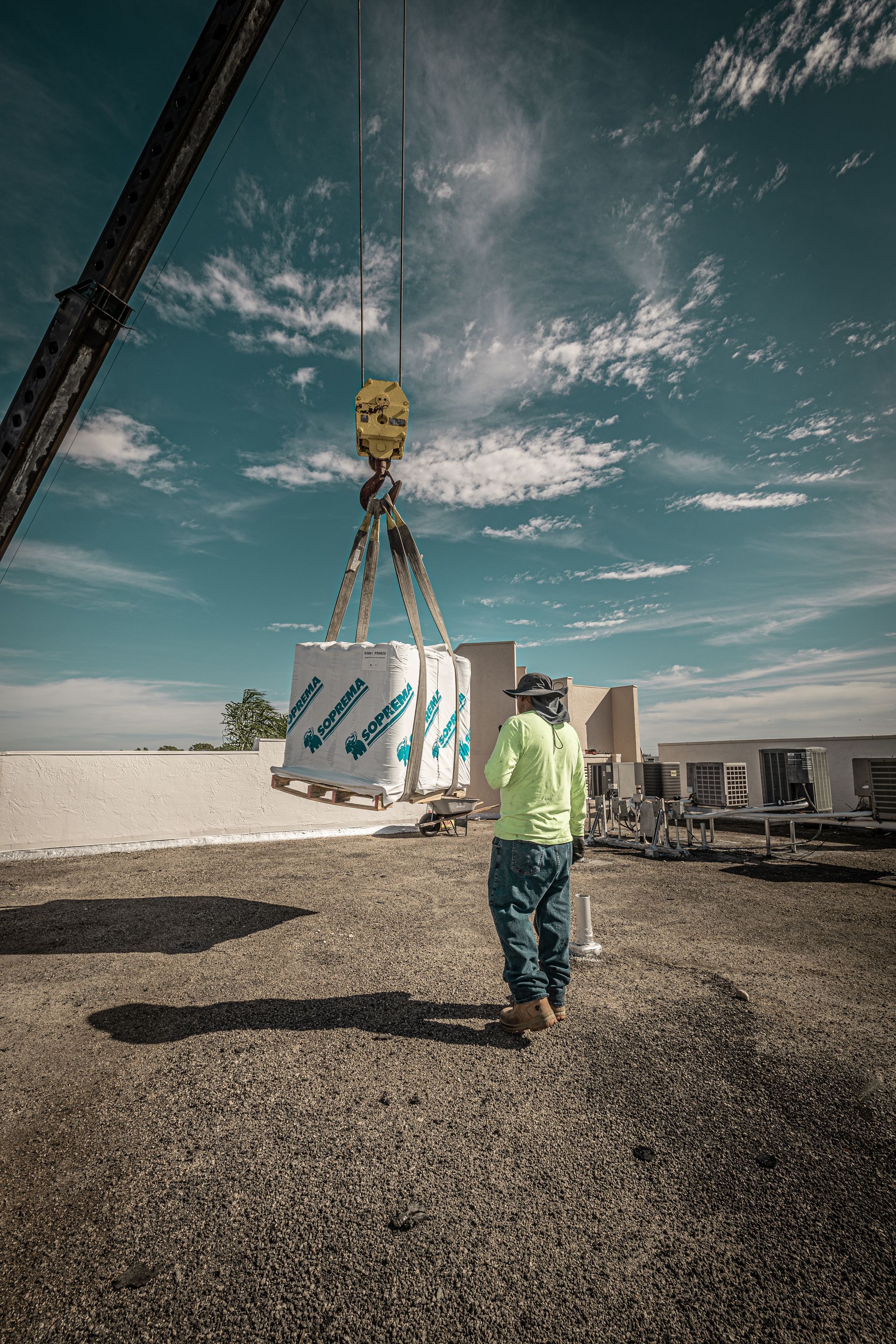 A man is walking towards a crane that is lifting a box.
