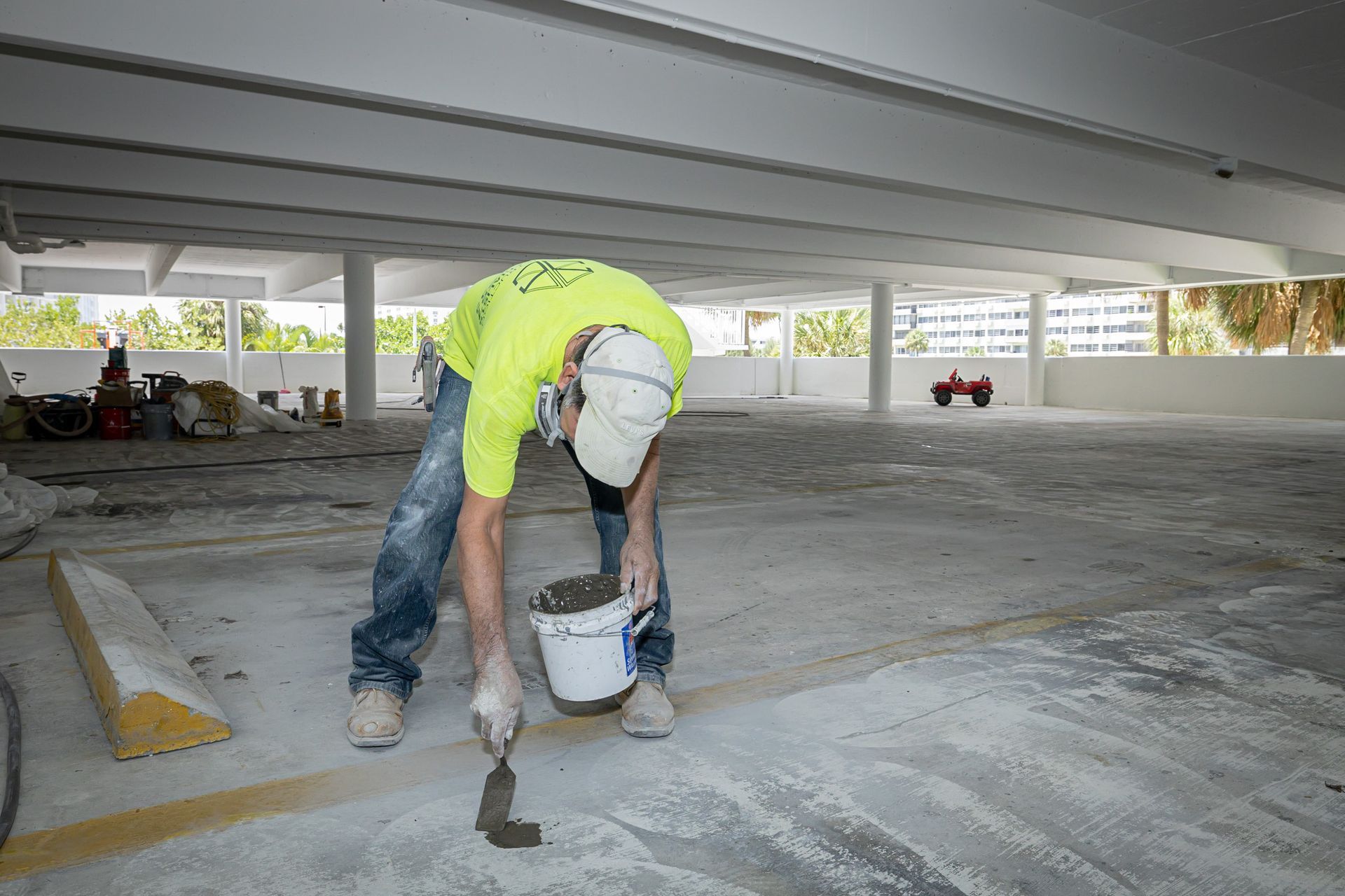 A man is painting a parking garage floor with a trowel.