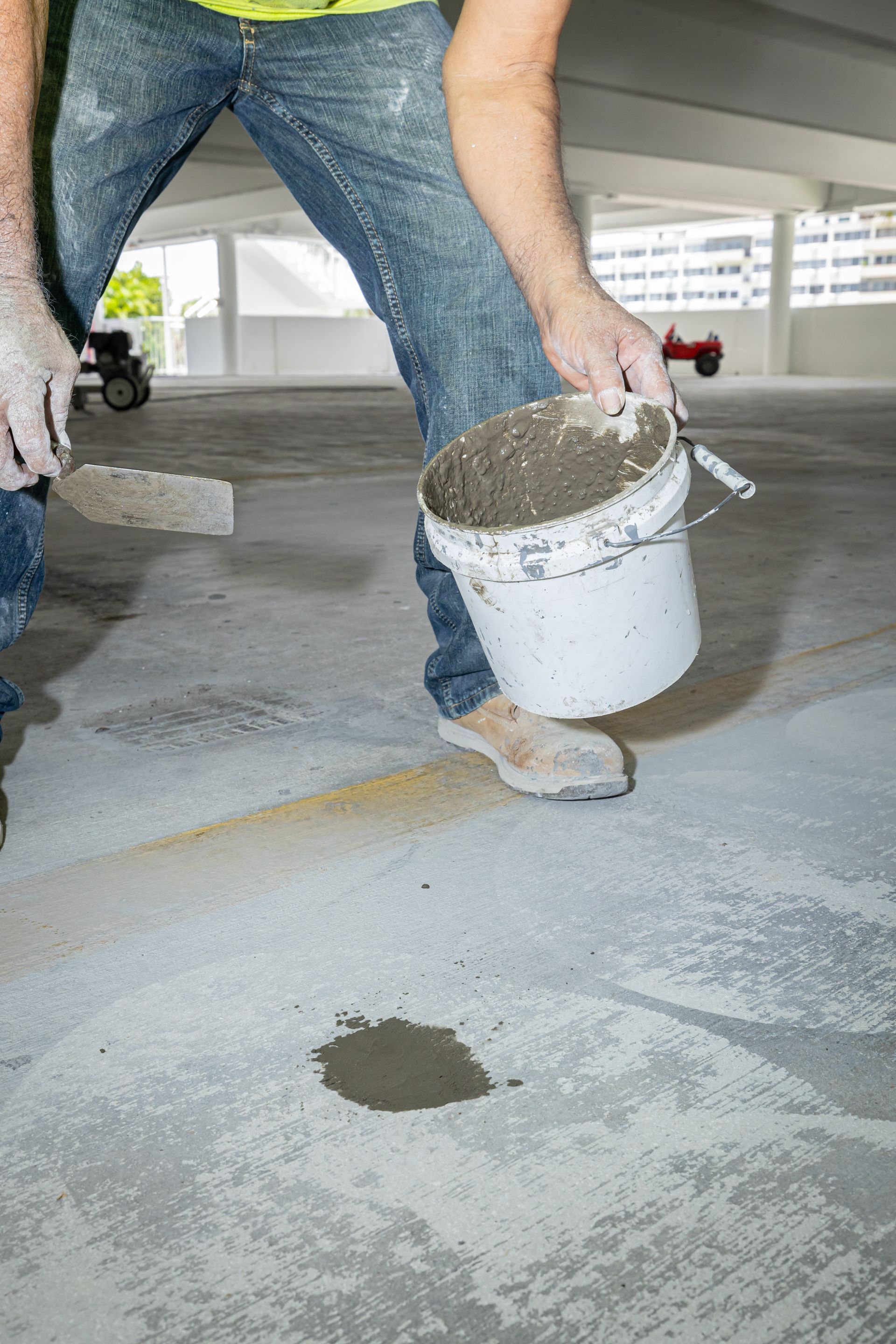 A man is holding a bucket of cement in a parking garage.