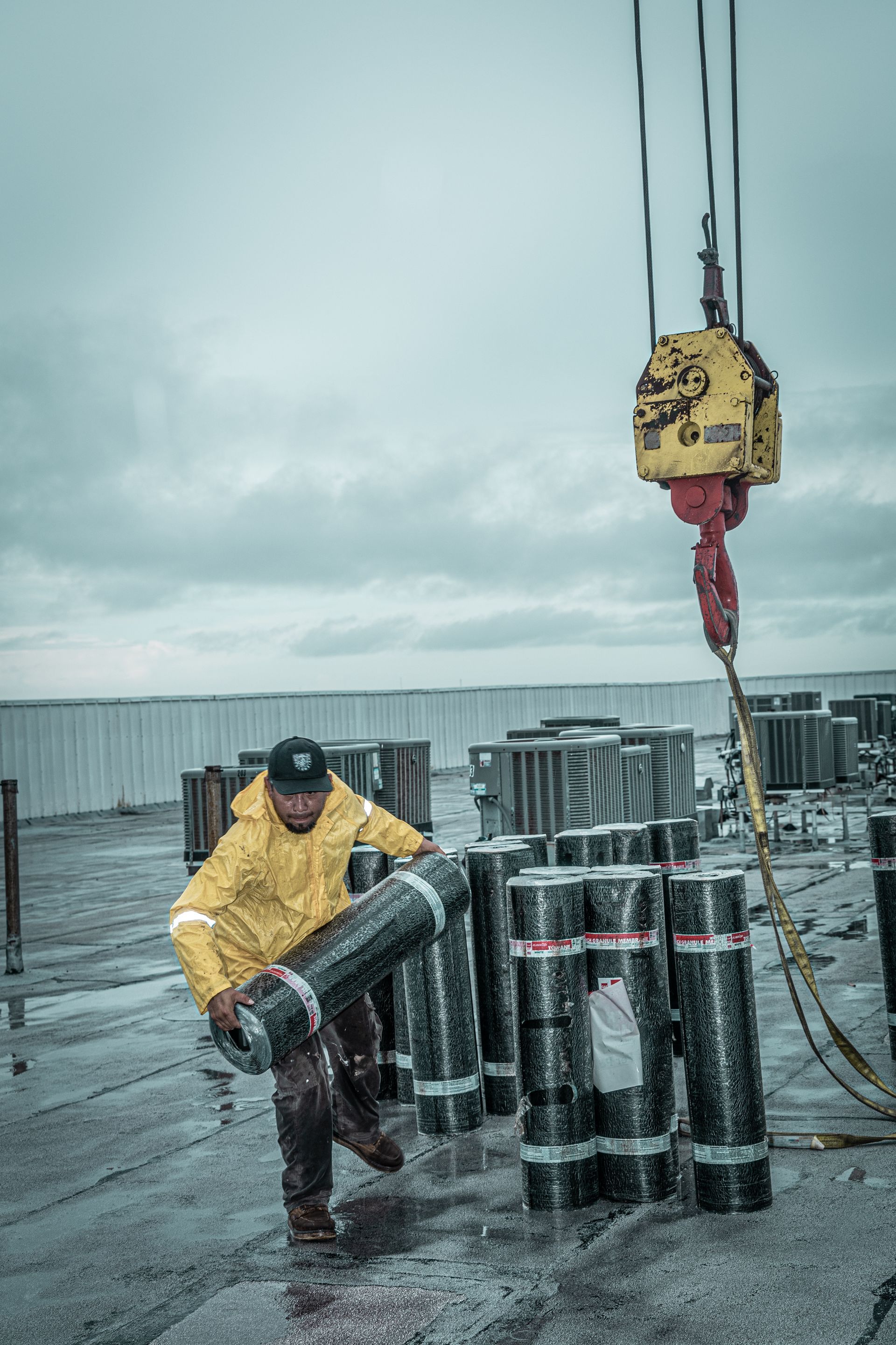 A man in a yellow jacket is carrying a roll of roofing material.