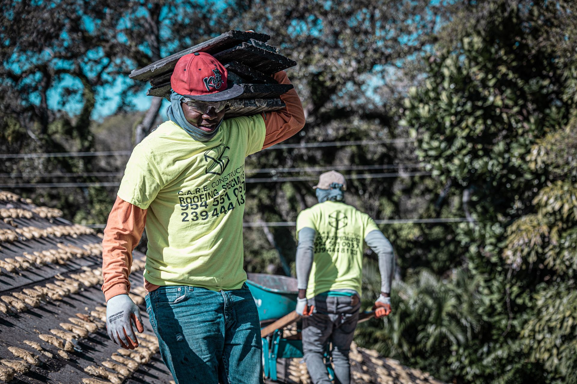 Two men are working on a roof and one of them is carrying a large piece of wood on his head.