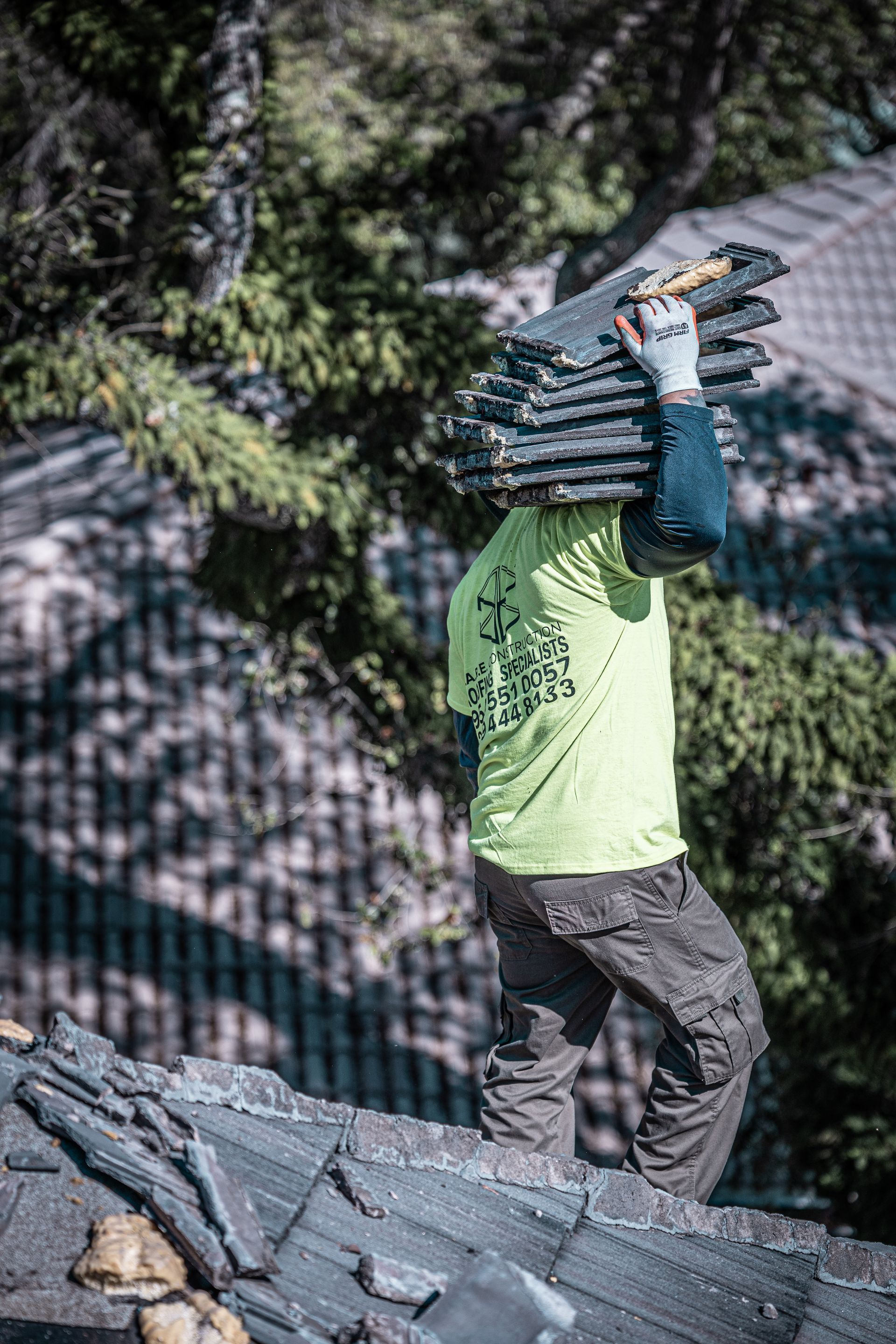 A man is carrying a stack of shingles on his head while standing on top of a roof.