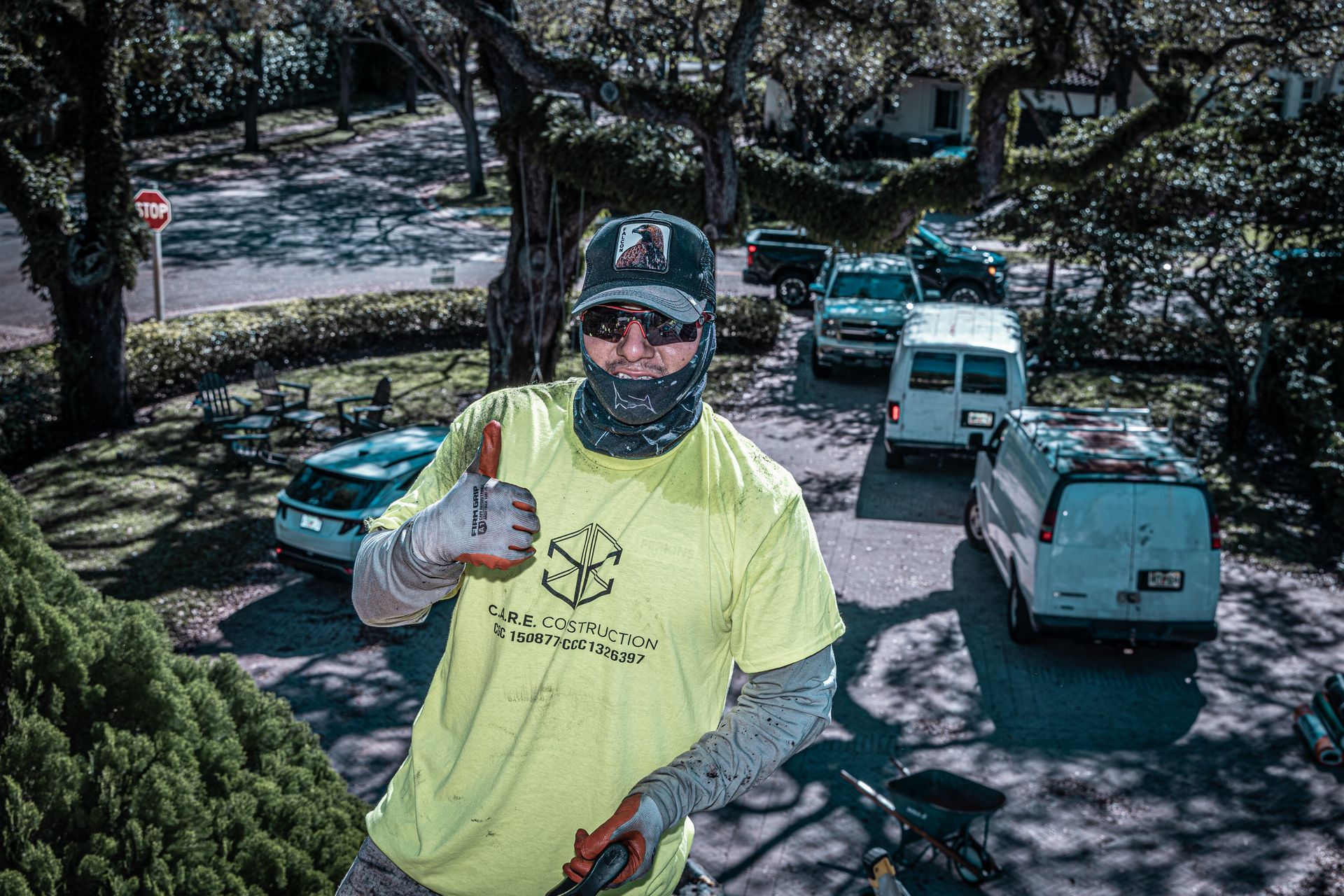A man wearing a yellow shirt and a mask is standing in front of a tree.