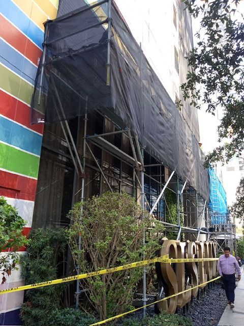 A man is walking down a sidewalk in front of a building with scaffolding on it.