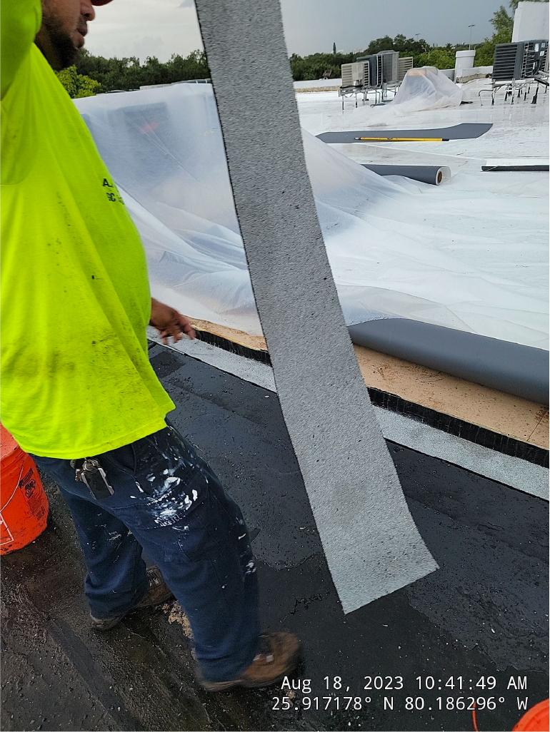 A man in a yellow shirt is holding a piece of plastic on a roof.