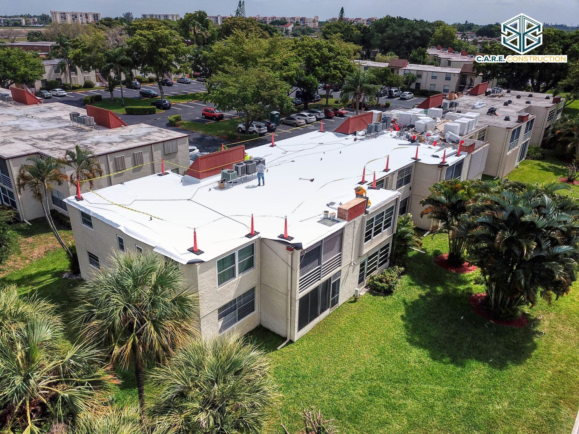 An aerial view of a large apartment building with a white roof surrounded by trees.