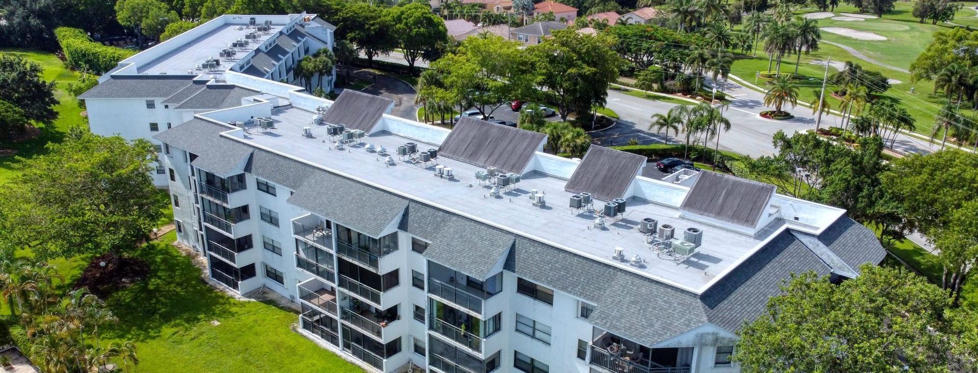 An aerial view of a large apartment building with solar panels on the roof surrounded by trees.