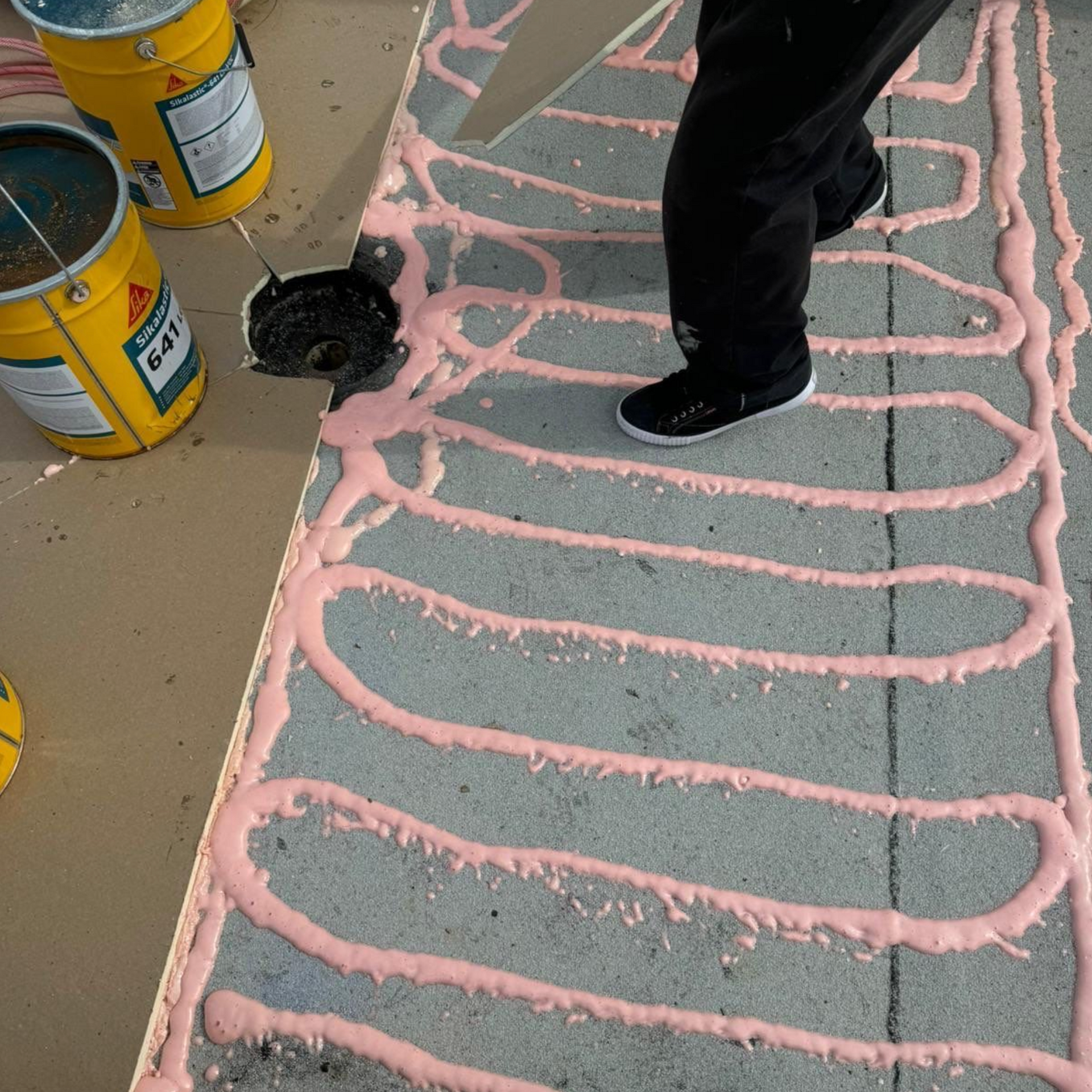 A person is spreading pink sika glue on a sidewalk