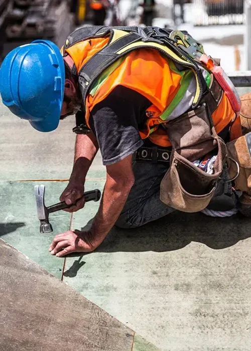 A construction worker is kneeling down on the ground holding a hammer.