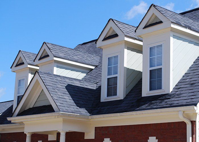 The roof of a house with three windows and a blue sky in the background.