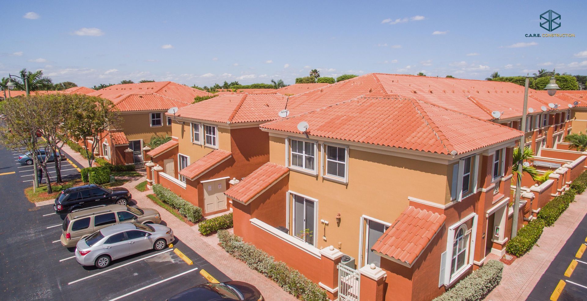 An aerial view of a row of houses with red tile roofs and cars parked in front of them.