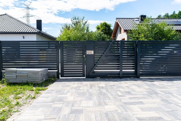 Gray metal fence and gate in front of a house. The driveway has gray patterned pavers.