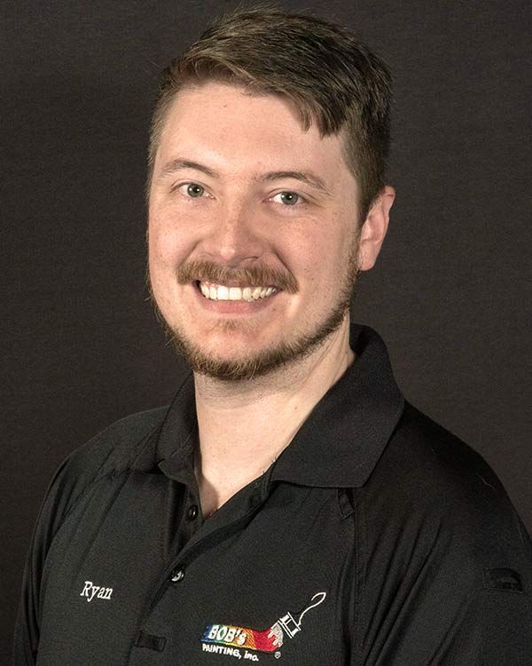 A man with a beard is wearing a black polo shirt and smiling.