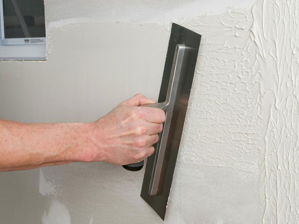A person is plastering a wall with a trowel.